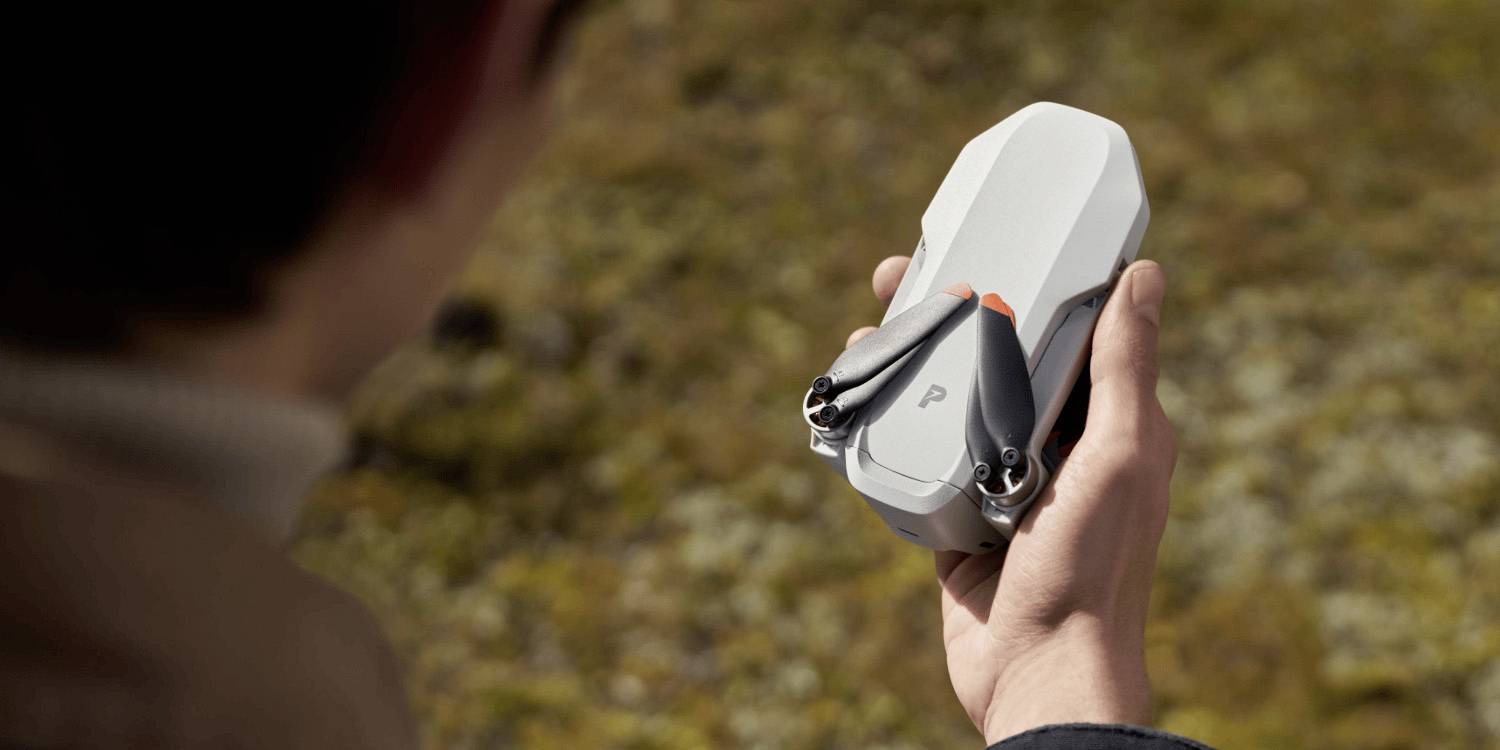 A person holding a compact, folded drone outdoors, preparing for flight over a grassy landscape.