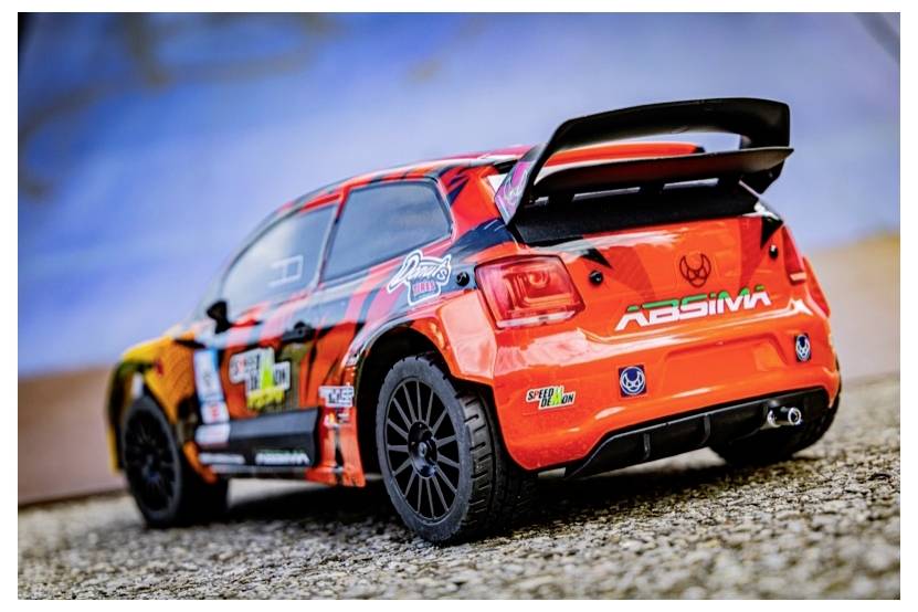 A vibrant toy racing car with orange, black, and red designs, parked on a textured surface, showcasing detailed decals and a rear spoiler.