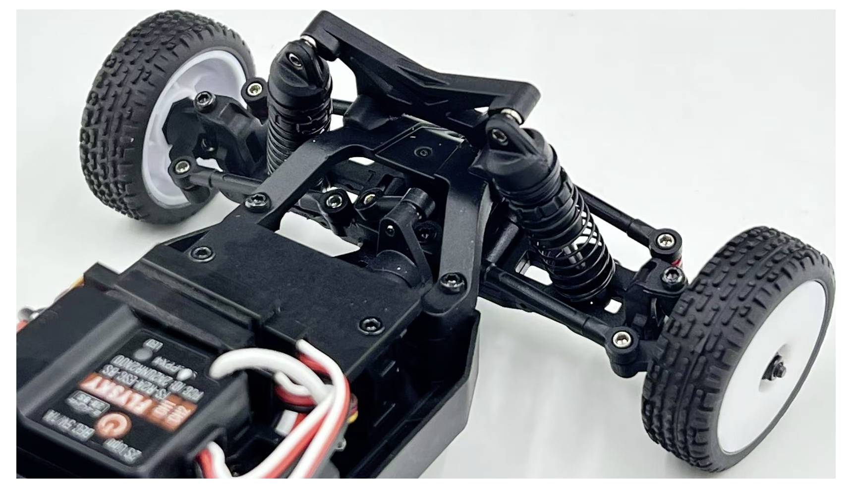 A close-up of a remote control car's chassis, highlighting its suspension system and wiring, set against a neutral background.
