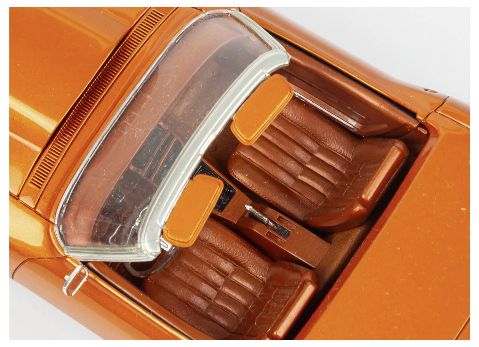 Top view of a miniature orange convertible car model, showcasing two brown seats and detailed interior features.