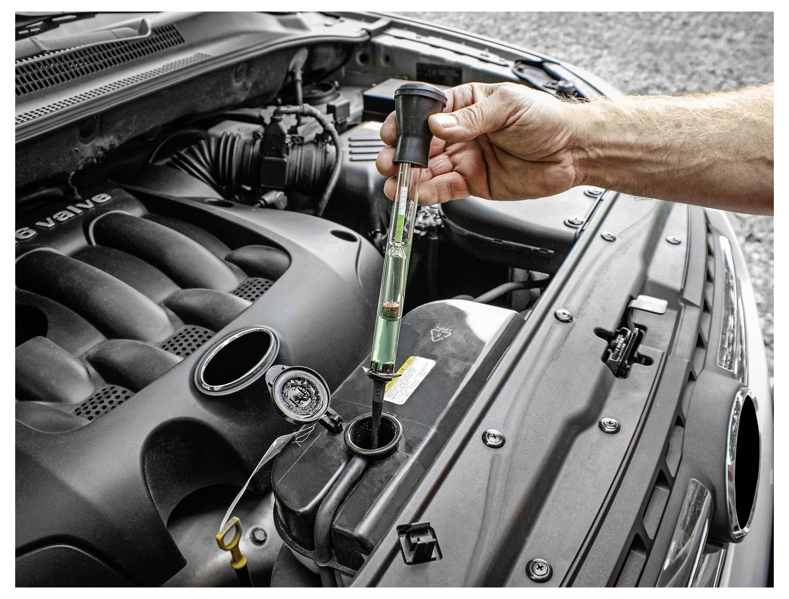 A person uses a hydrometer to check the radiator fluid in a car engine, illustrating routine vehicle maintenance.
