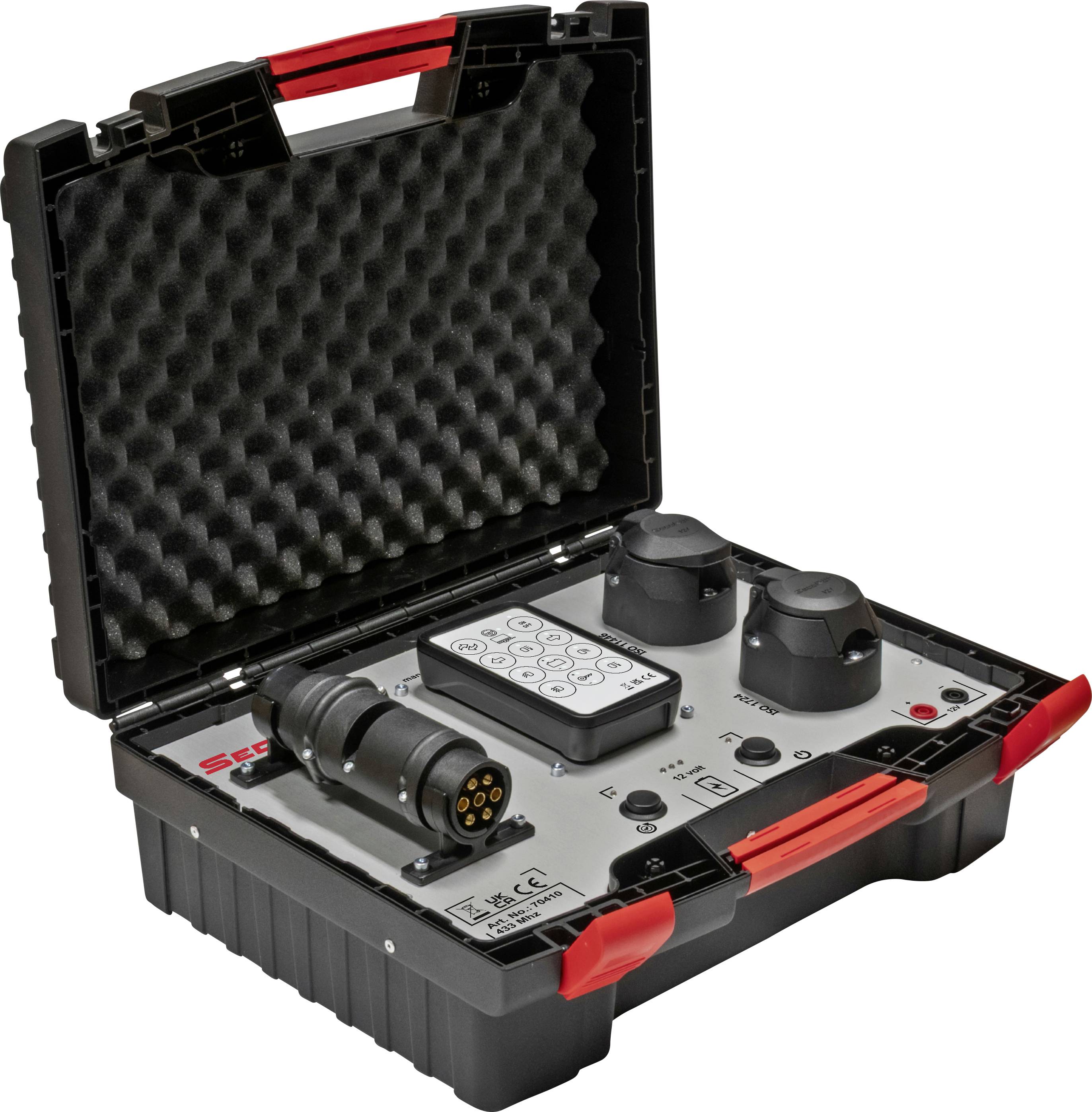 A portable electronic testing device in a protective case with a foam lid, featuring connectors, buttons, and a numeric keypad.