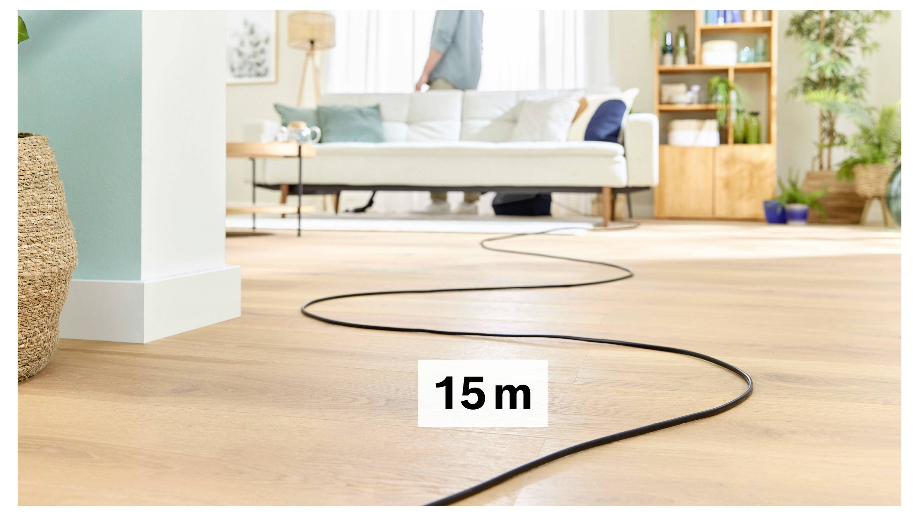 A 15-meter black cable is stretched across a wooden floor in a bright living room, leading towards a white couch with plants around.