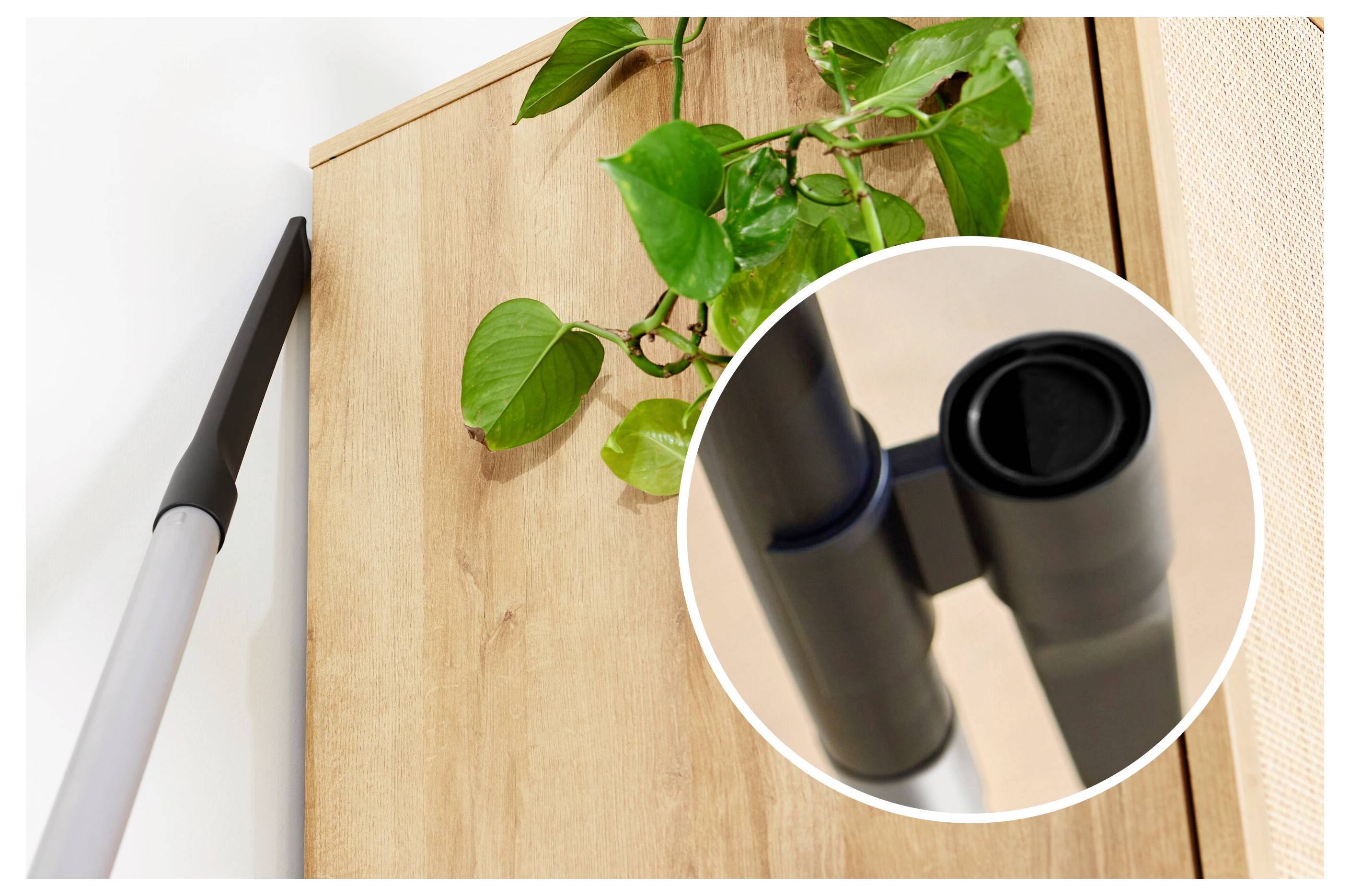 A vacuum cleaner nozzle reaching a high cabinet corner, with an inset showing the nozzle tip. A plant is on top of the cabinet.