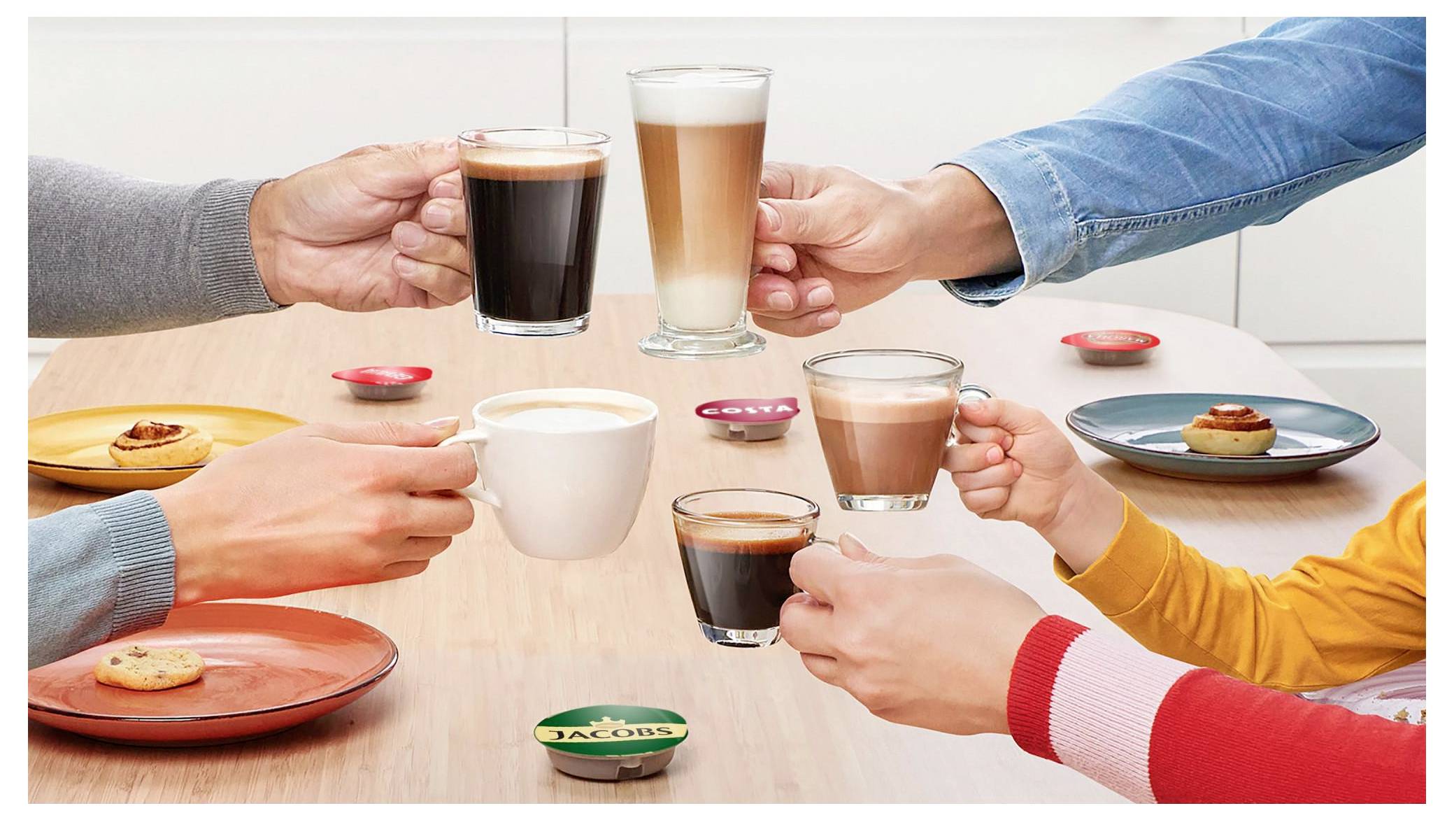 Hands holding different types of coffee drinks in cups over a wooden table with saucers and cookies, depicting a coffee gathering.