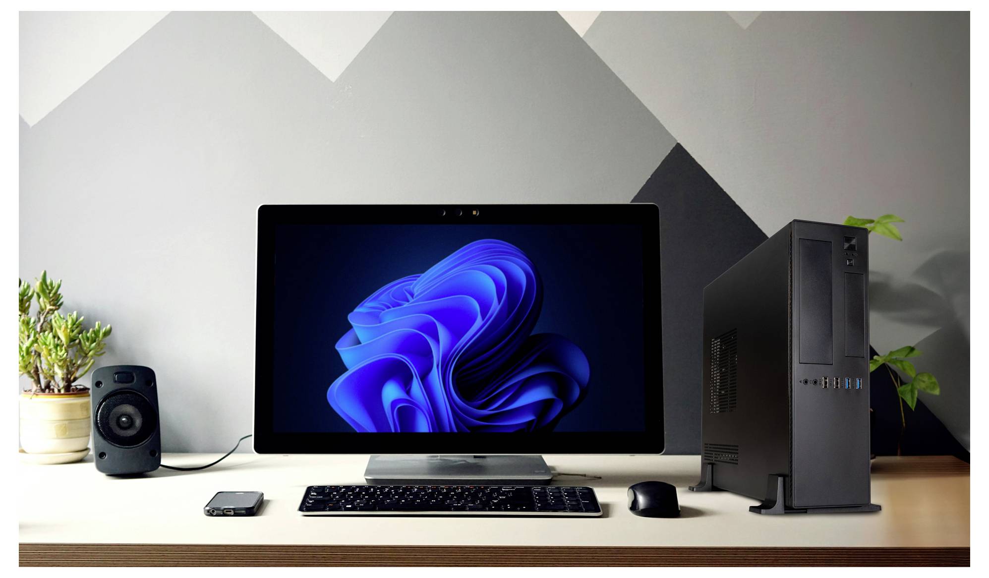 A tidy desk with a computer monitor displaying a blue abstract design, a keyboard, mouse, smartphone, speaker, and desktop tower.
