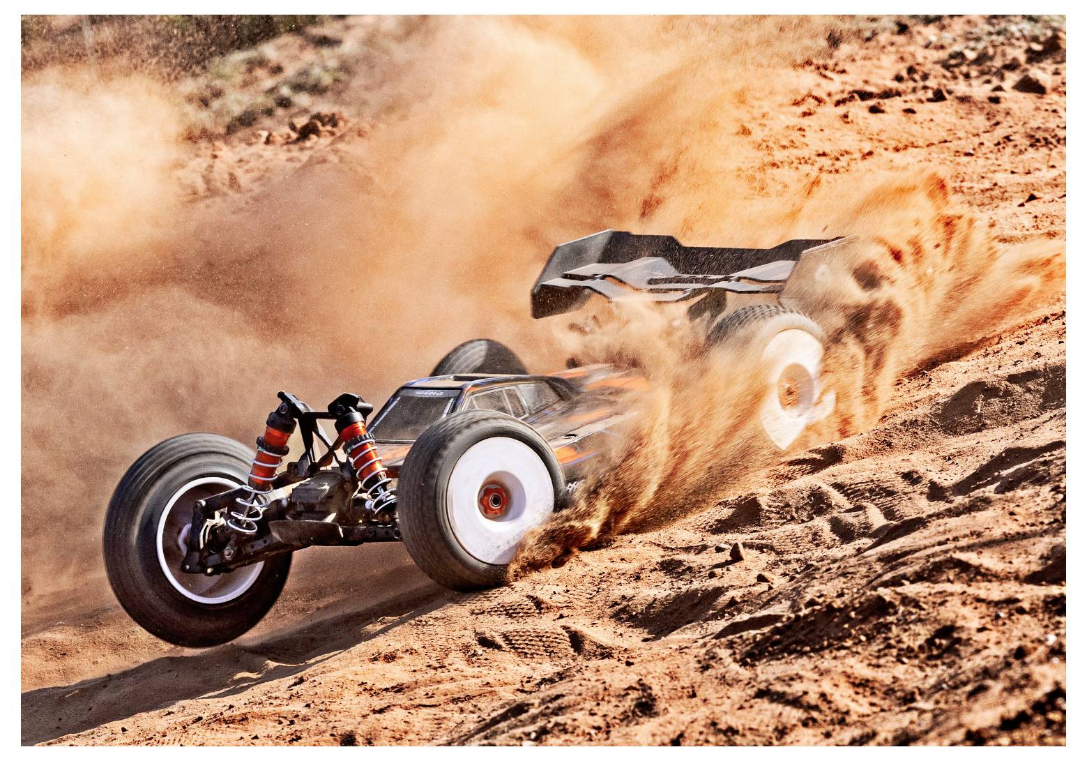 A remote-controlled car kicks up dust as it swiftly navigates a sandy terrain.