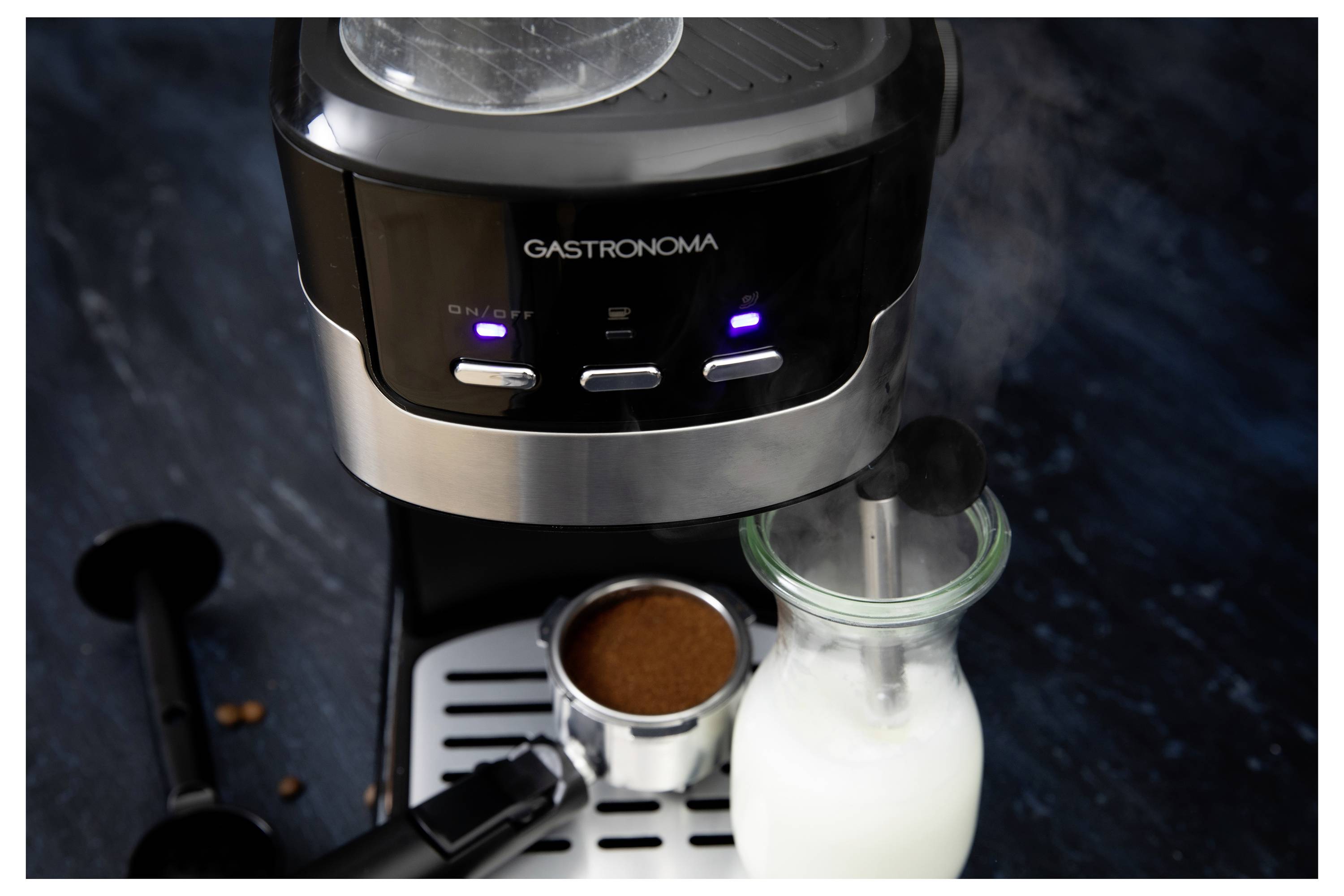 'Gastronoma' coffee machine on a counter with steamed milk in a glass bottle and a portafilter filled with ground coffee.