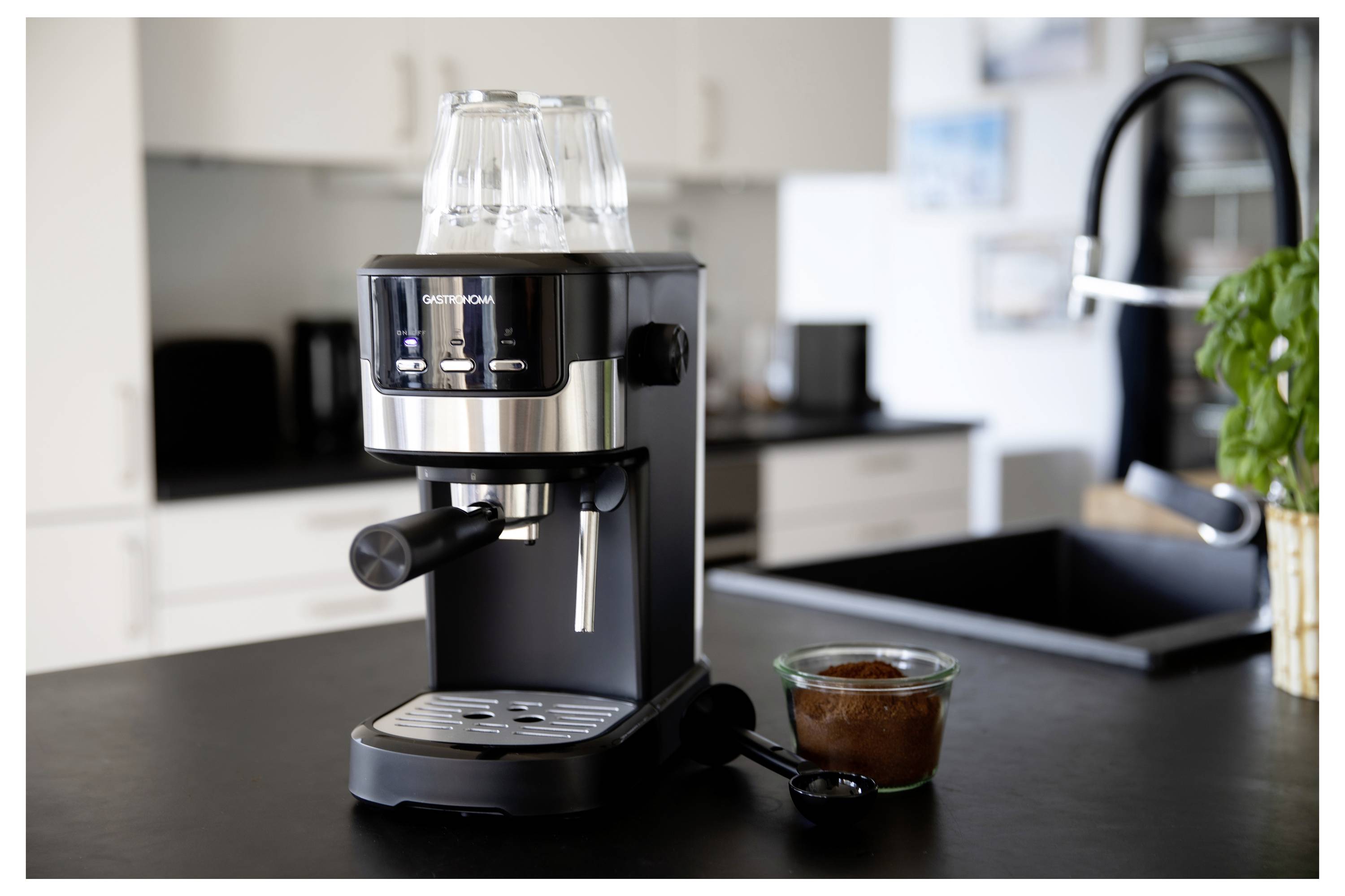 A black and stainless steel espresso machine on a kitchen counter with a cup of ground coffee and stacked cups on top of the machine.