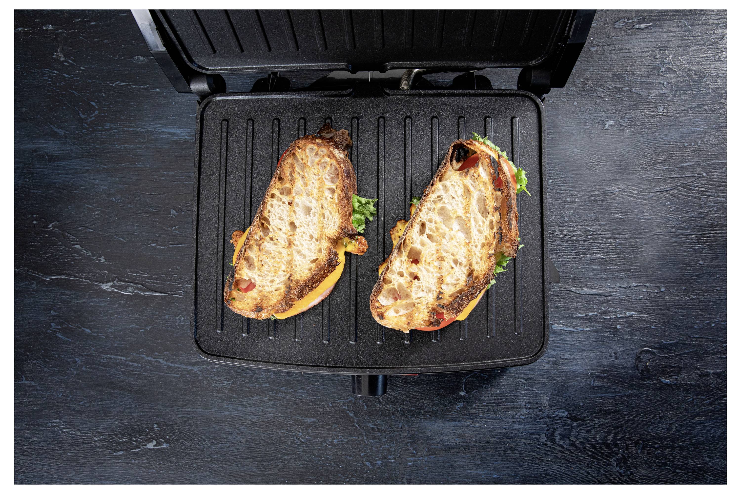 Two toasted sandwiches with melted cheese and vegetables on a black grill pan.