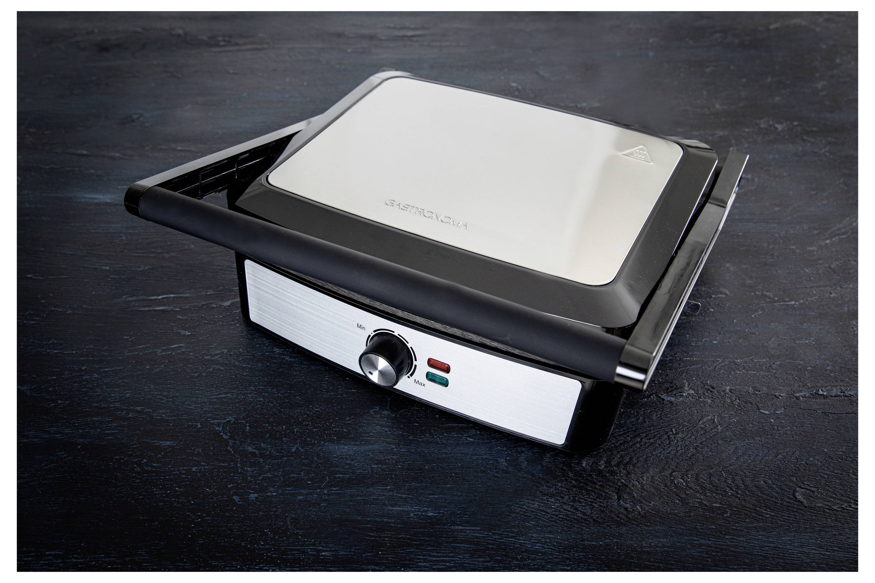 A closed silver and black electric grill sits on a dark surface. The grill has a knob for temperature control and indicator lights.