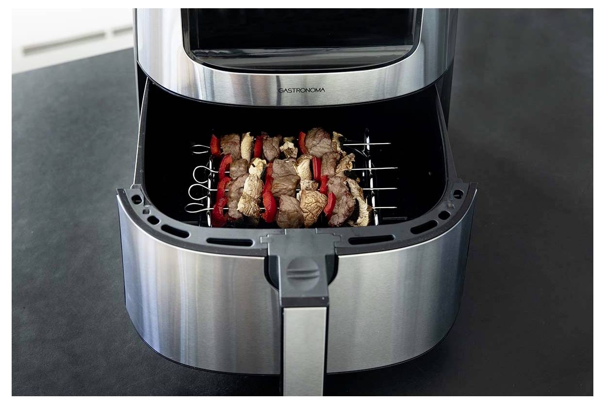 An air fryer with skewers of meat and vegetables inside, ready for cooking, set on a dark kitchen countertop.