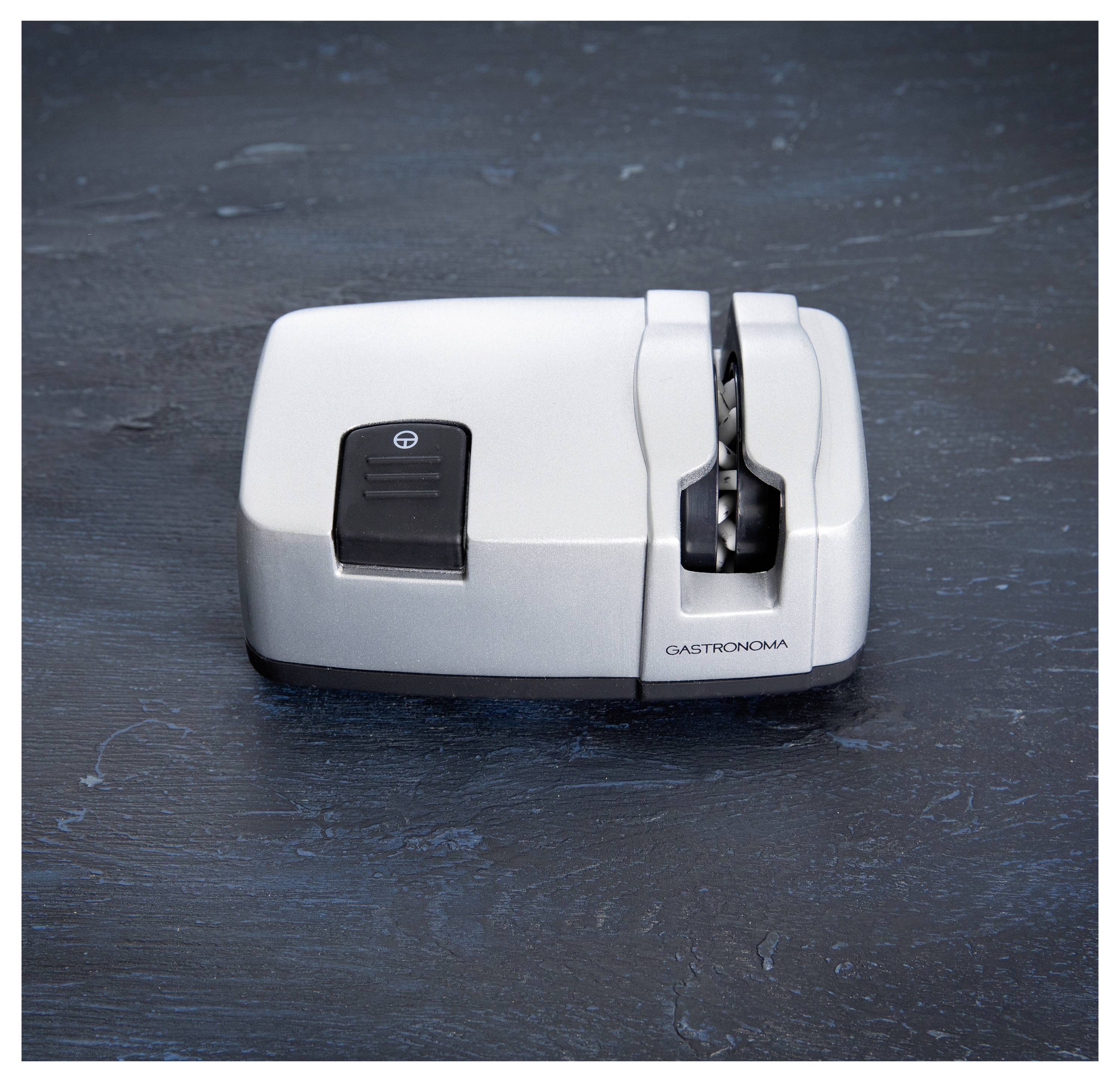 Electric knife sharpener on a dark surface with slots for honing and sharpening blades.