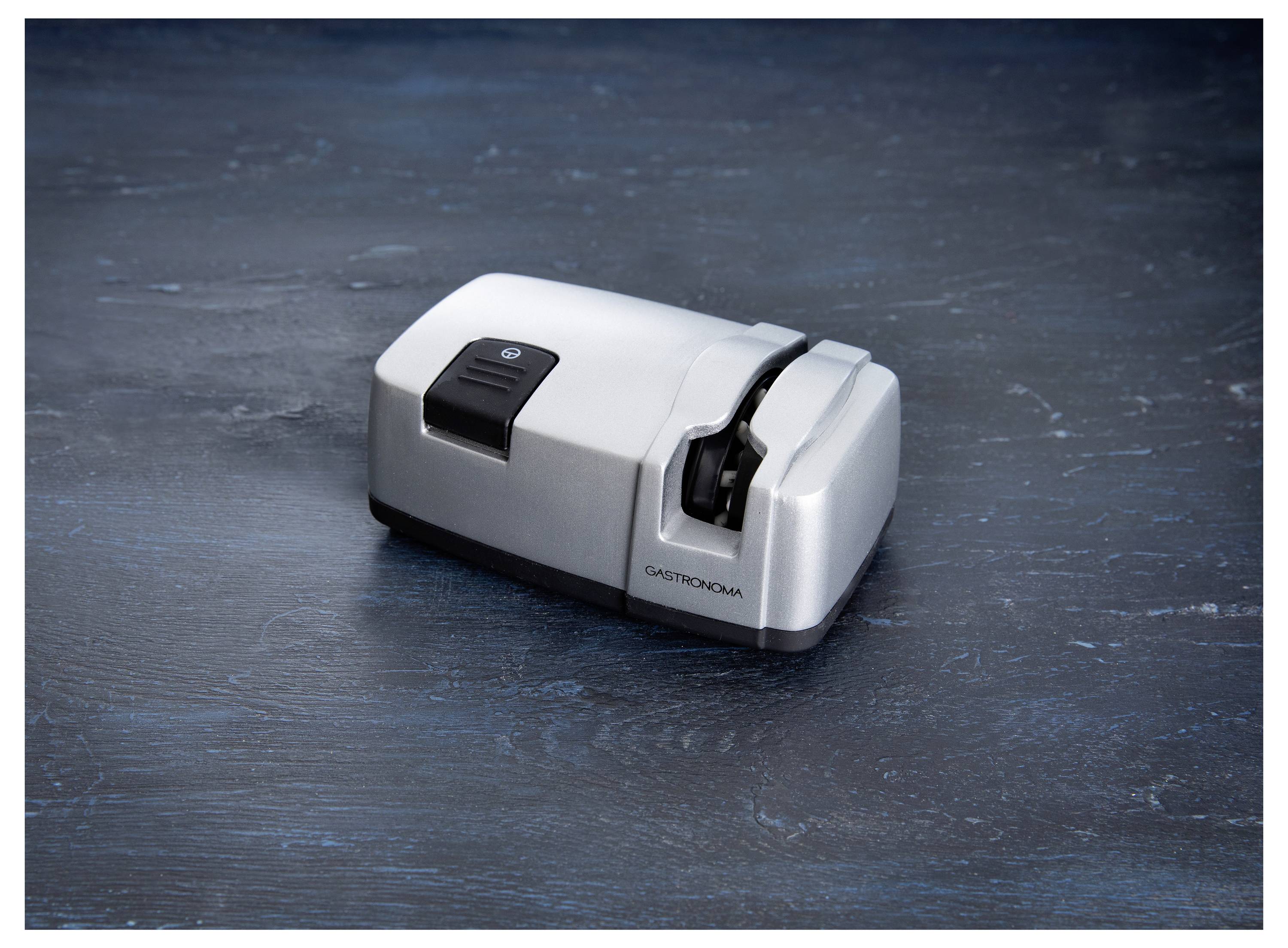 Image of a silver electric knife sharpener with a visible power button and logo on a dark textured surface.