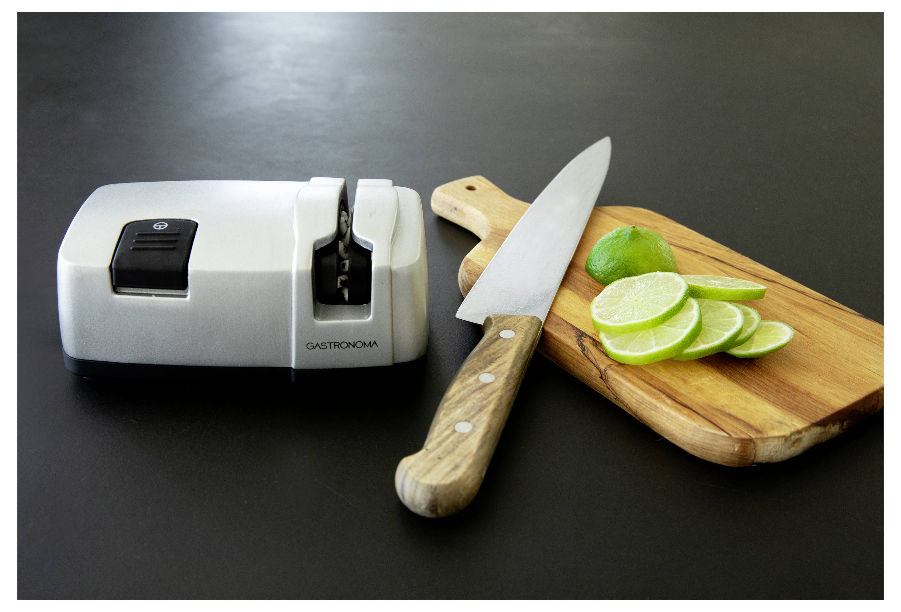 A knife sharpener next to a wooden cutting board with a knife and sliced limes on a dark countertop.
