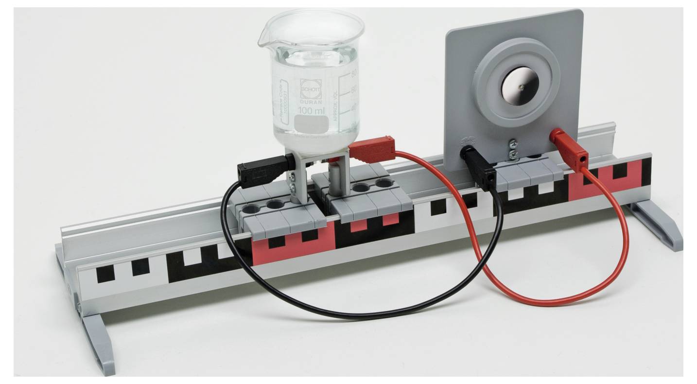 An electric circuit setup with a beaker, a metal plate, and wires connecting to a power source, illustrating a conductivity experiment.