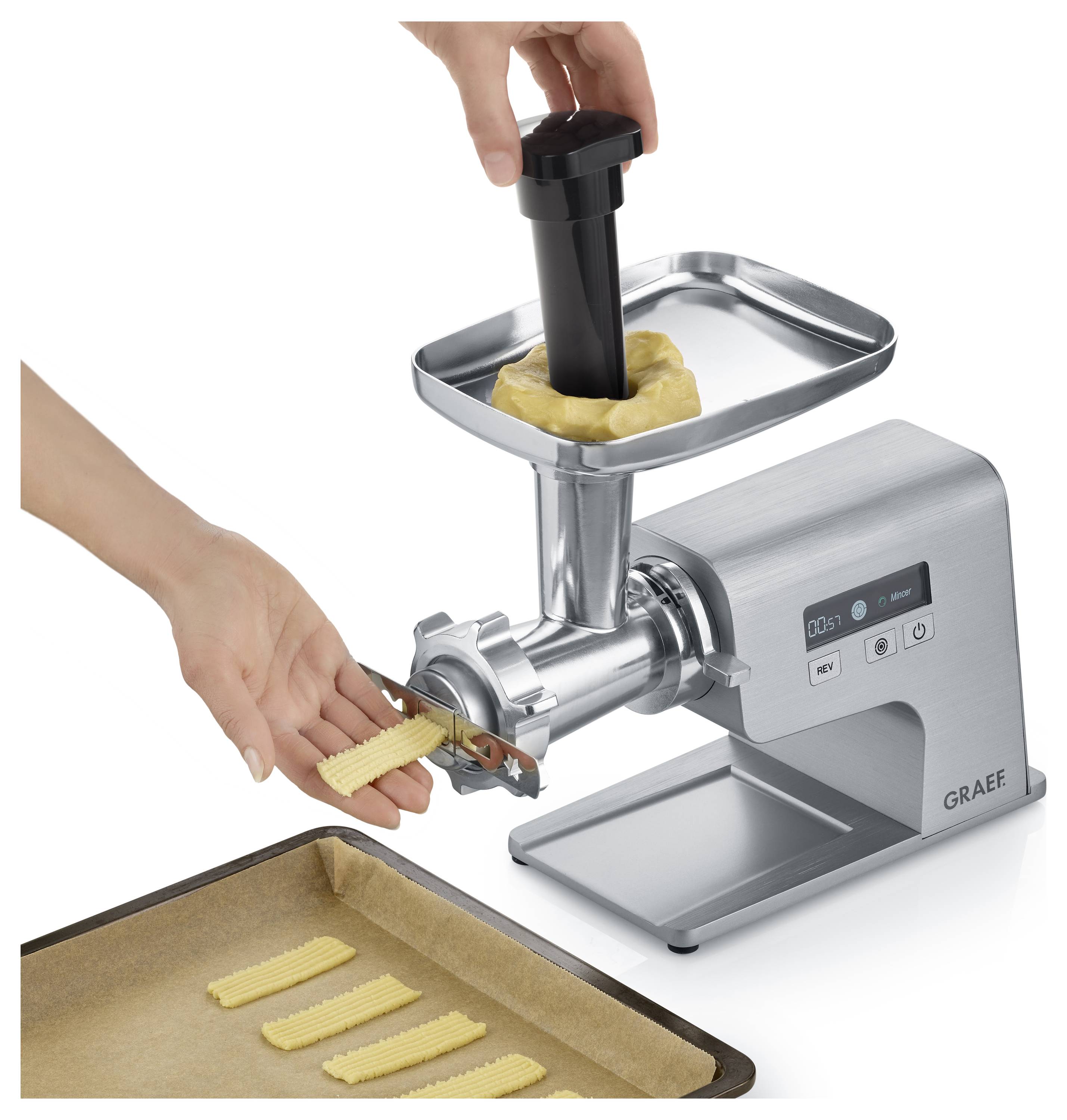 A person uses a metal cookie press to shape dough into strips on a baking tray, showing the process of preparing cookies.