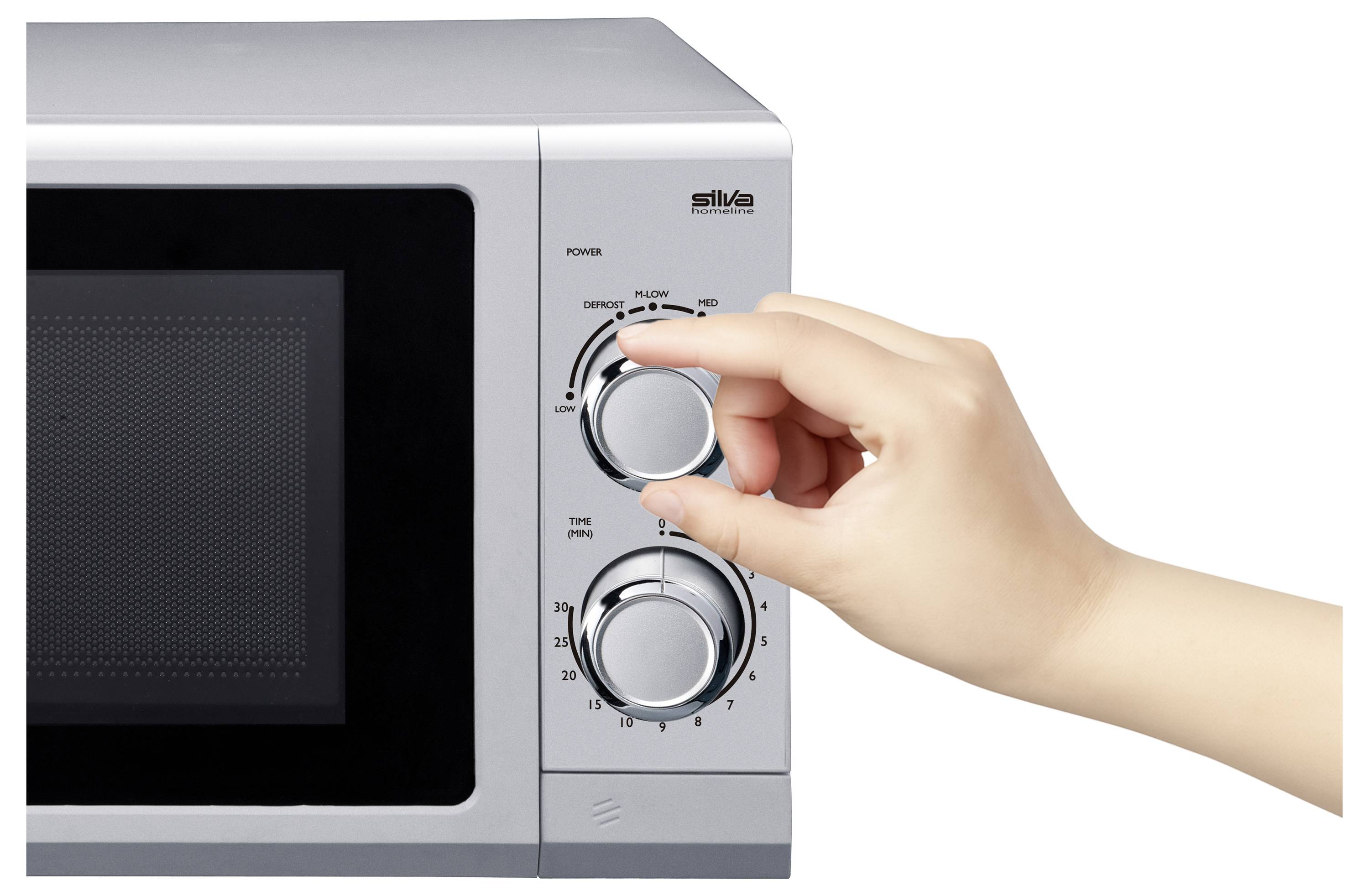 A person adjusts the timer knob on a microwave oven, setting it to 10 seconds. The silver appliance features a power knob above the timer.