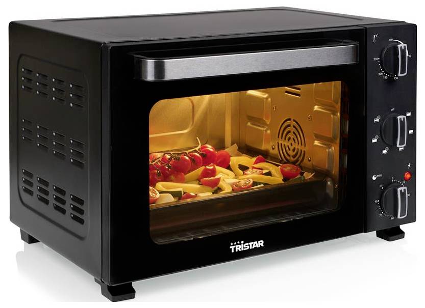 A black countertop oven with a transparent door shows vegetables baking inside. Three control knobs are on the right side.