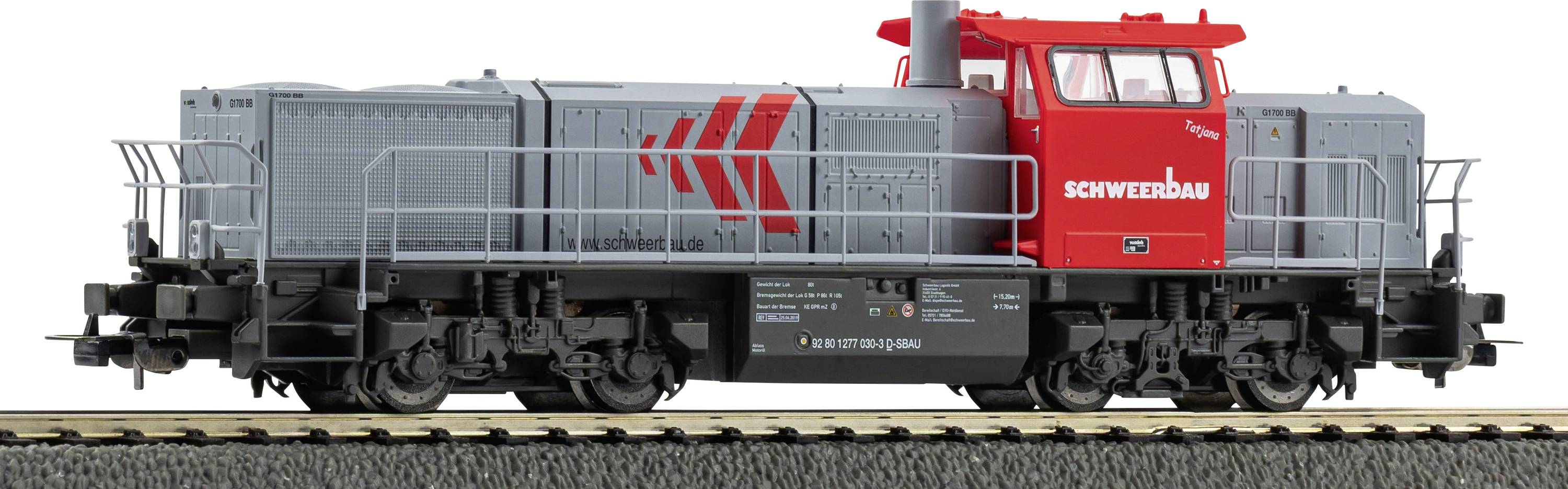 A model train engine in gray and red with 'SCHWERER' logo on the side, on a display track, showcasing detailed rail and wheel components.