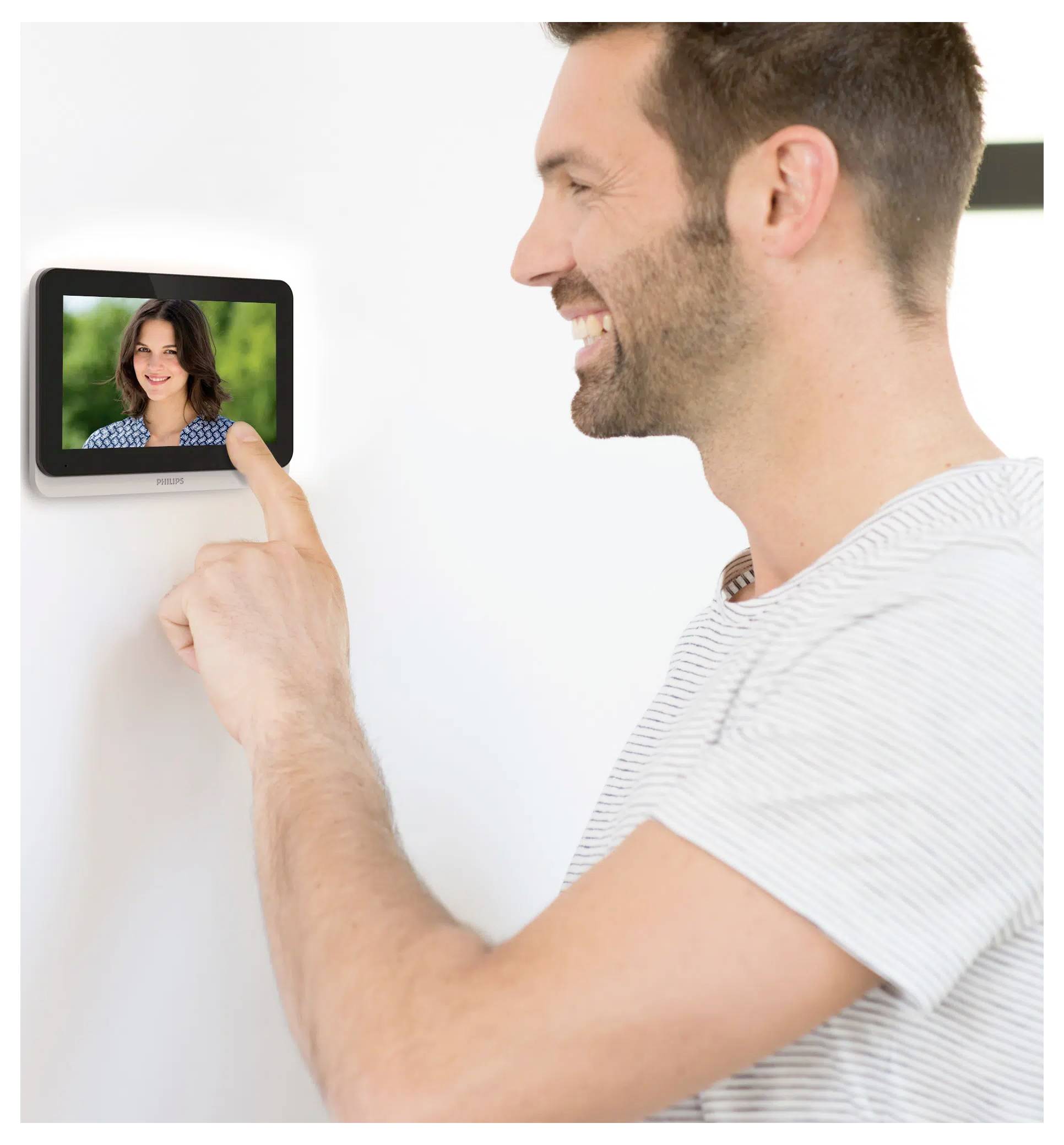 A person smiling and touching a wall-mounted video intercom screen displaying a woman smiling.
