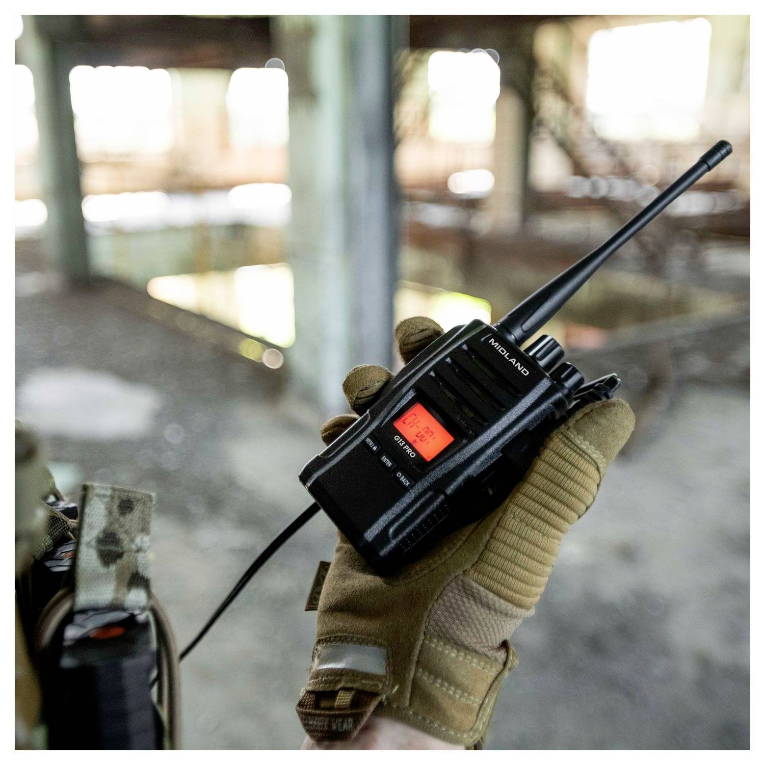 A person wearing tactical gloves holds a walkie-talkie indoors, emphasizing communication equipment in an industrial setting.