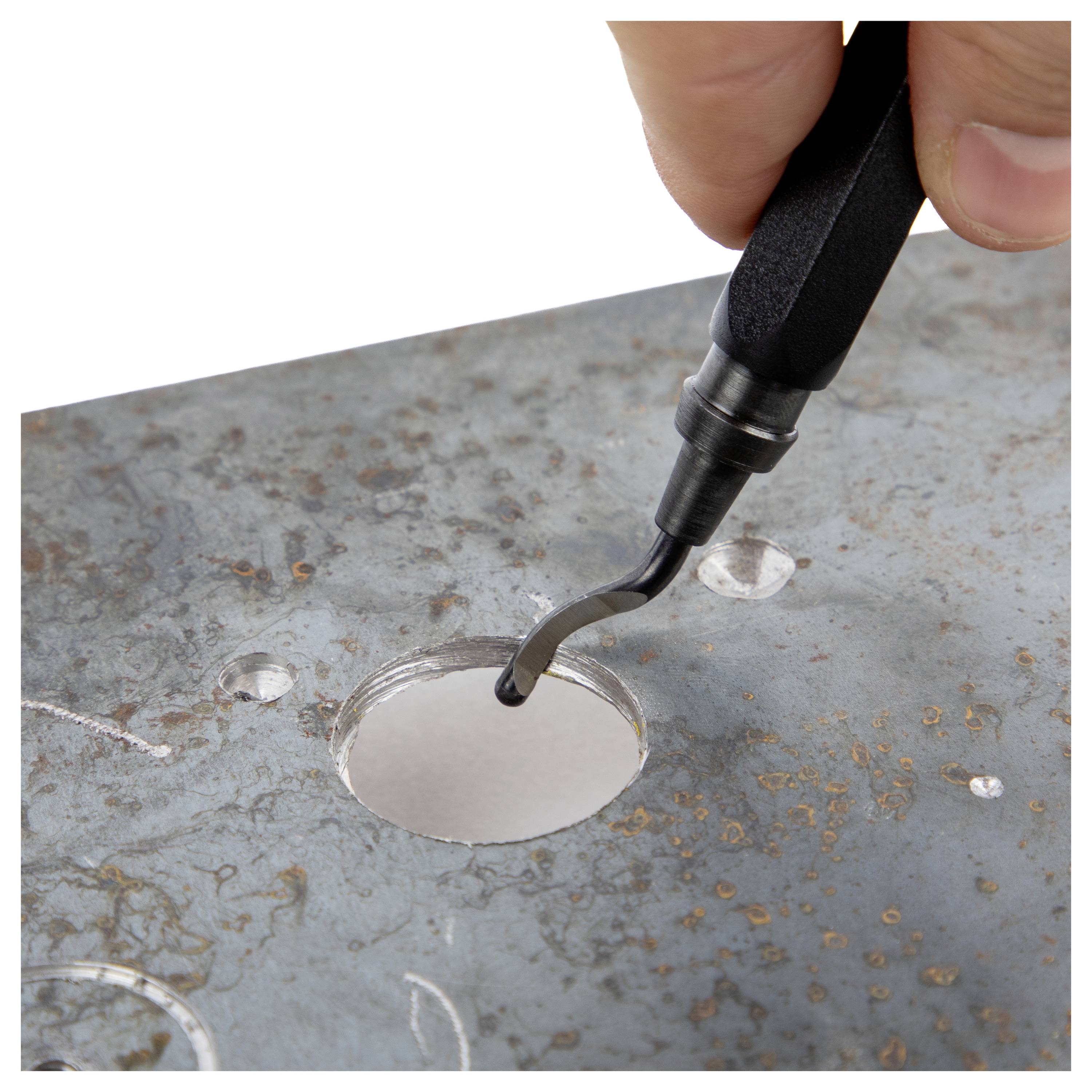 A hand uses a deburring tool to smooth the edges of a hole in a metal surface.