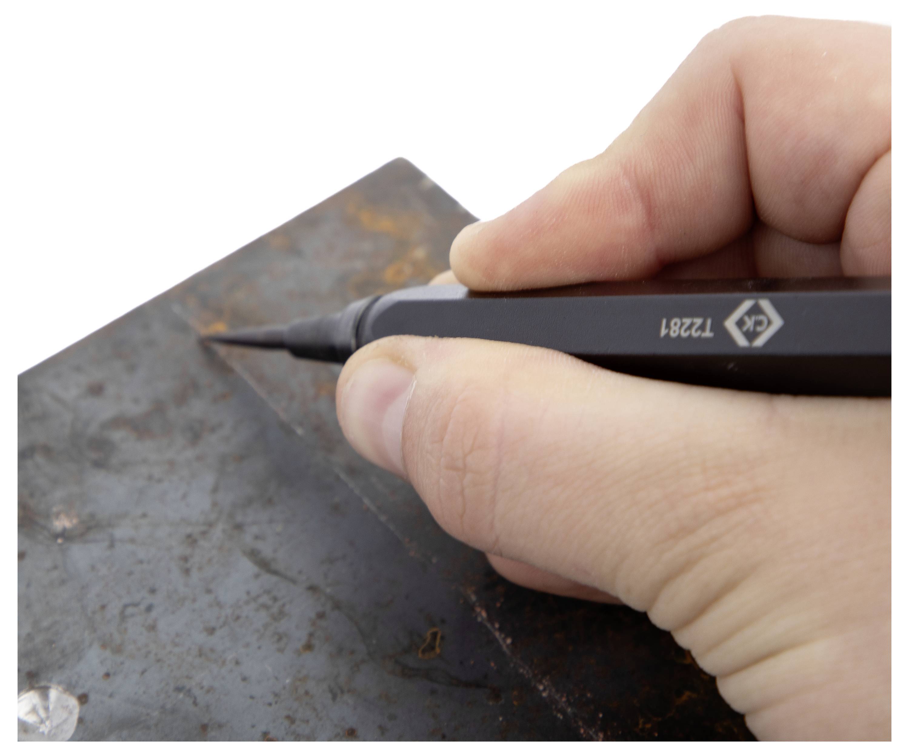 Close-up of a hand holding a precision tool, marking a rusted metal surface, suggesting measurement or crafting in progress.