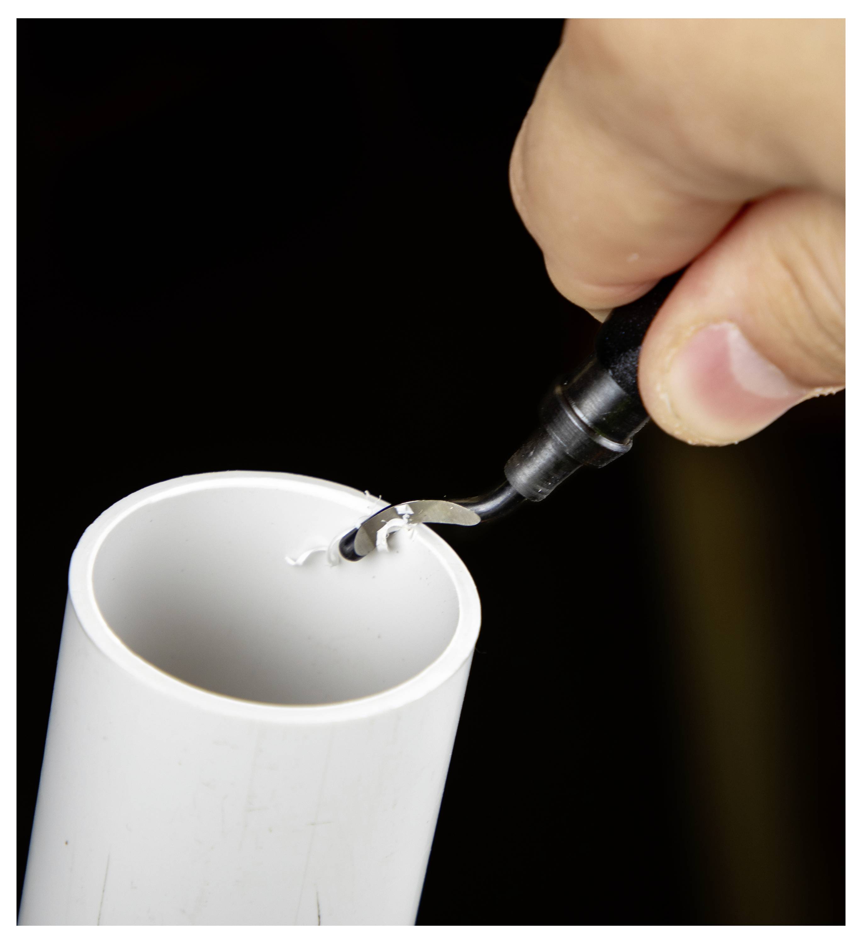 A hand holding a deburring tool is smoothing the edge of a cut white plastic pipe, removing excess material for a clean finish.