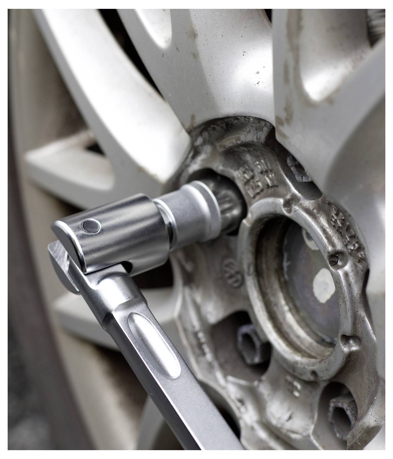 A tire being removed from a car using a socket wrench, showing the lug nuts being unscrewed from the wheel hub, close-up view.