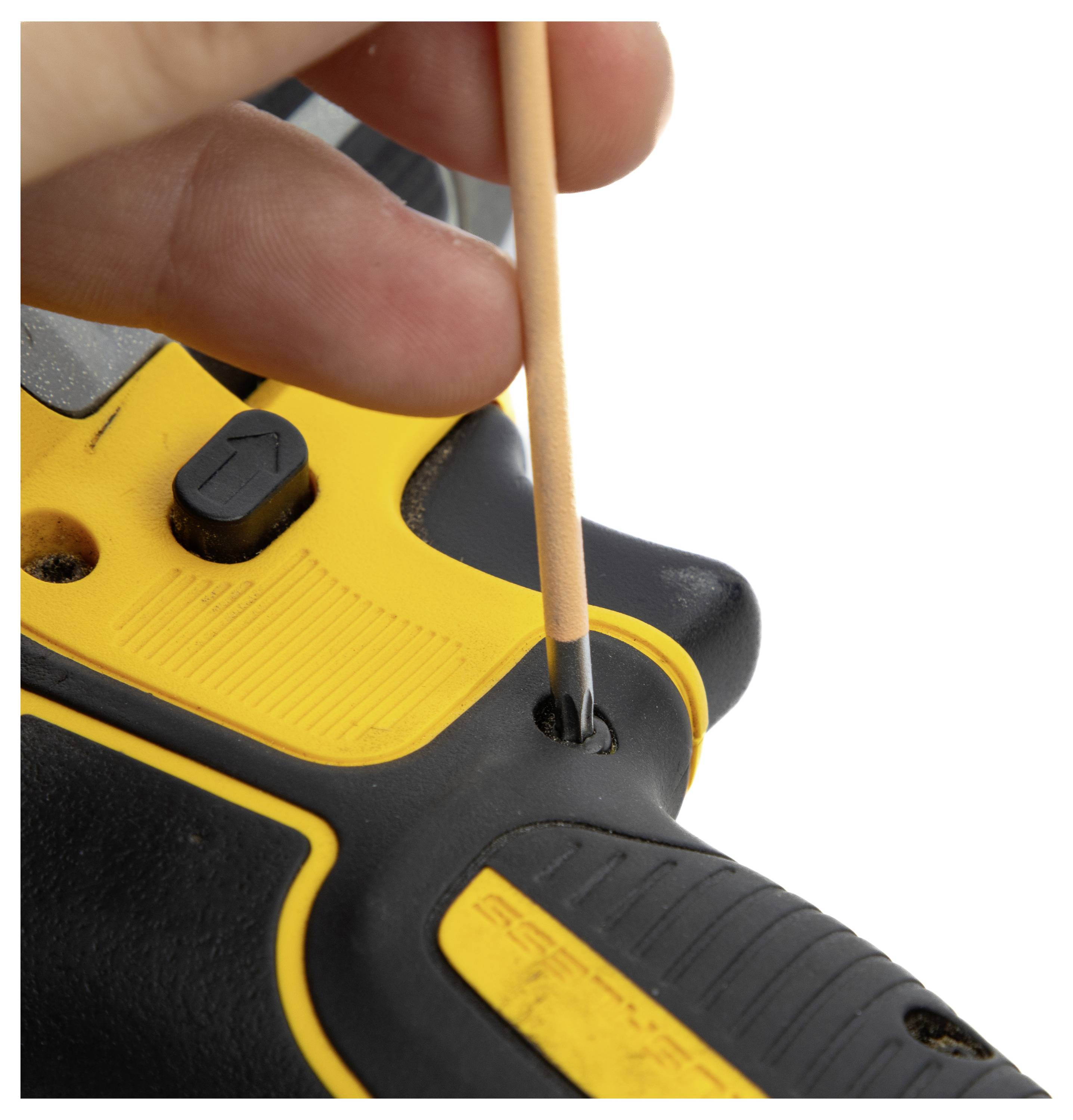 A hand using a small tool to adjust a yellow and black electronic device, focusing on a small hole near a control button.