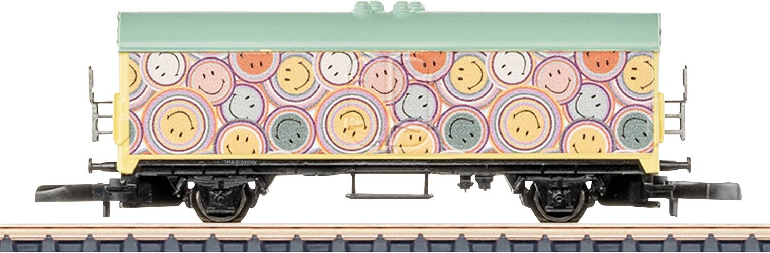 A colorful train carriage with a pattern of smiley faces and concentric circles on its sides, positioned on a train track.
