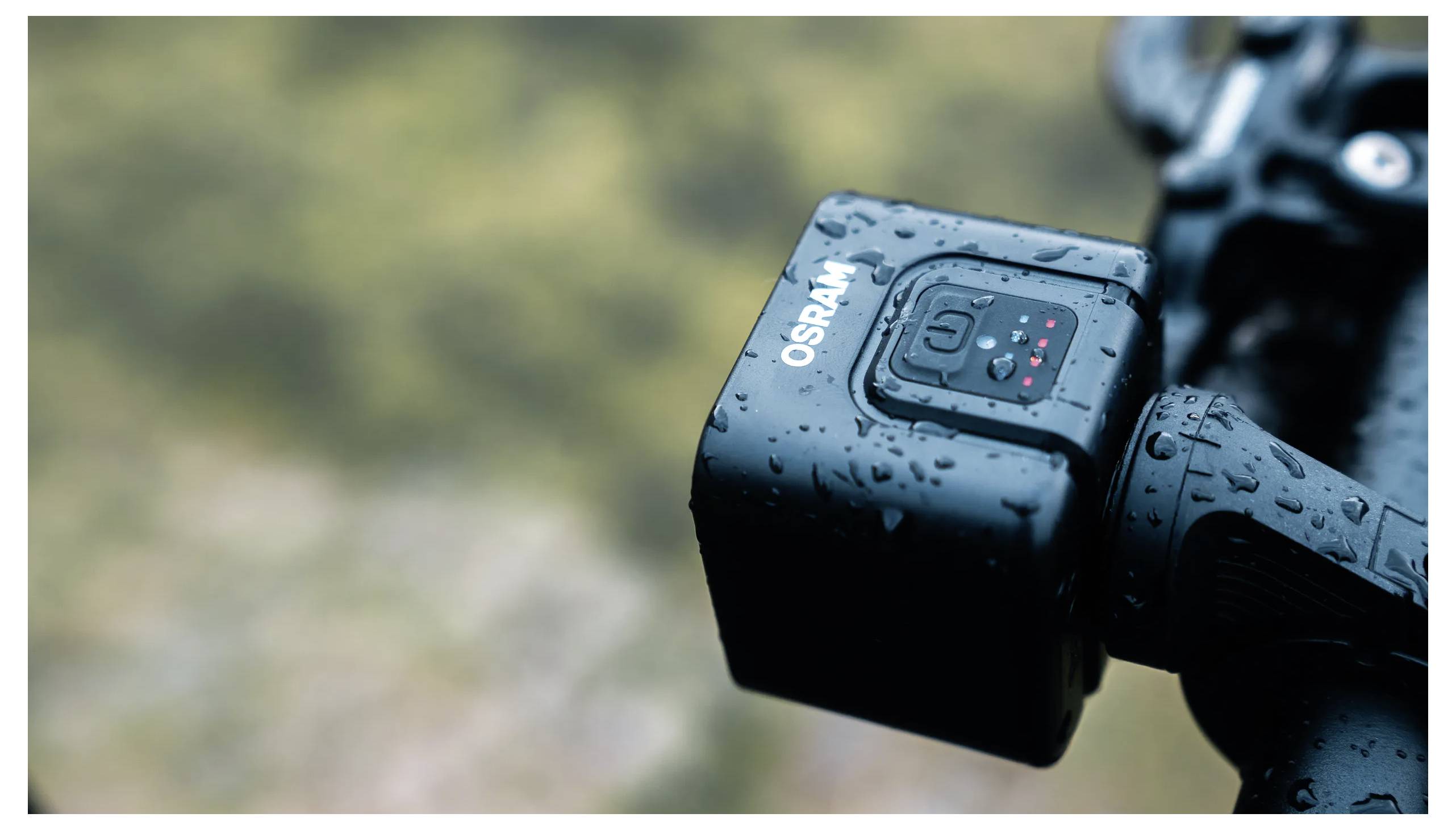 A small, rain-covered camera mounted on a handle, labeled 'OSRAM', with indicator lights visible against a blurred outdoor background.