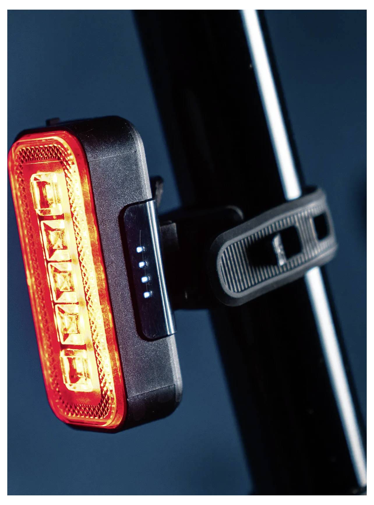 A red LED bike tail light attached to a black seat post, showing a glowing red light and a row of blue battery indicator lights.