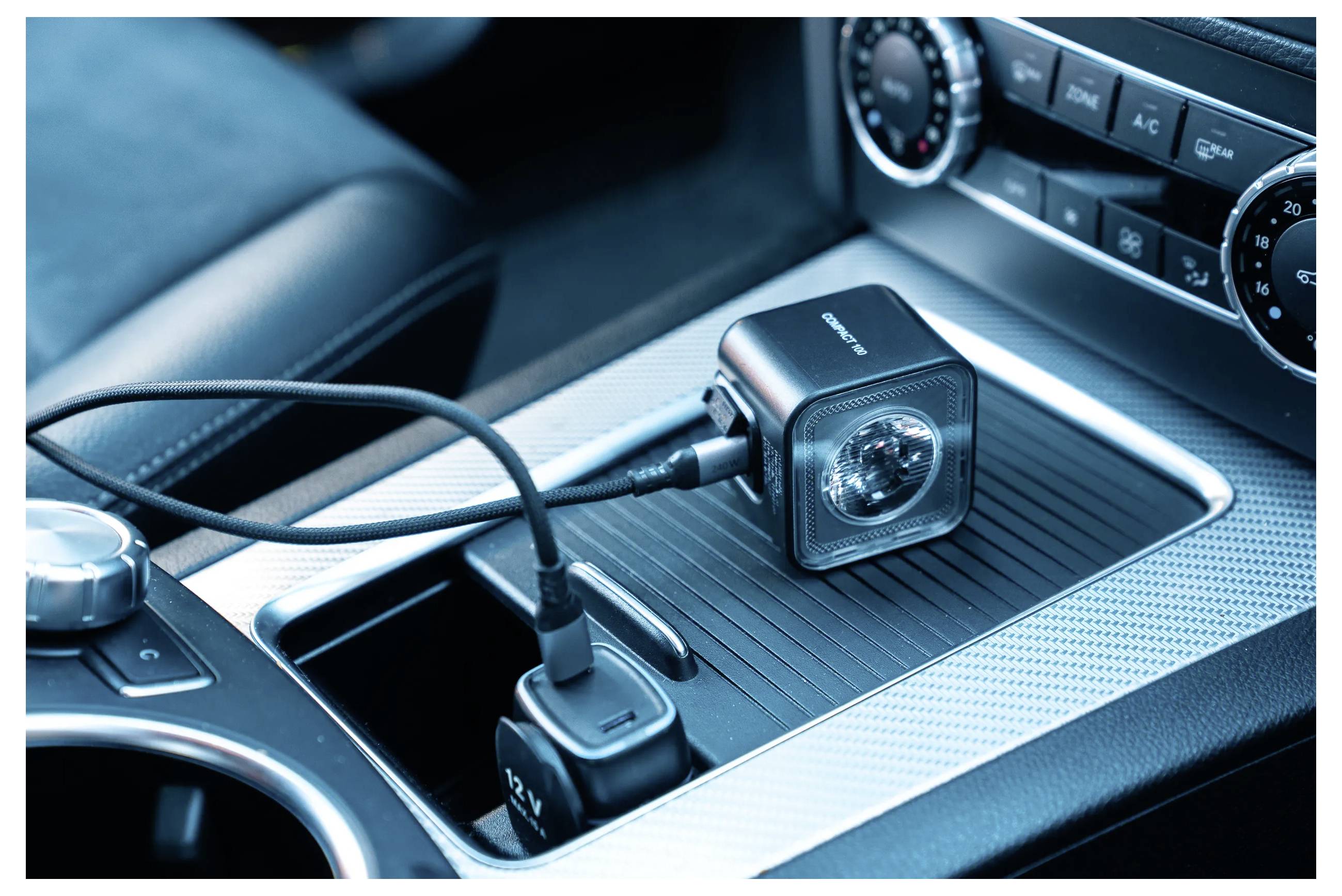 Car dashboard with dual USB charger plugged into cigarette lighter, powering a small, portable fan. Climate controls visible.