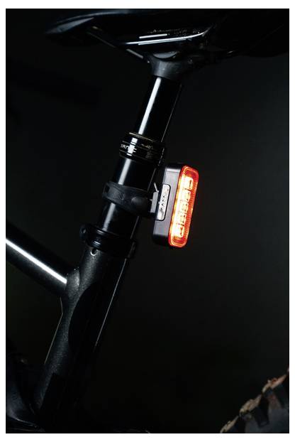 A bike seat and rear light at night, with the light illuminated in red, attached to the seat post of the bicycle.