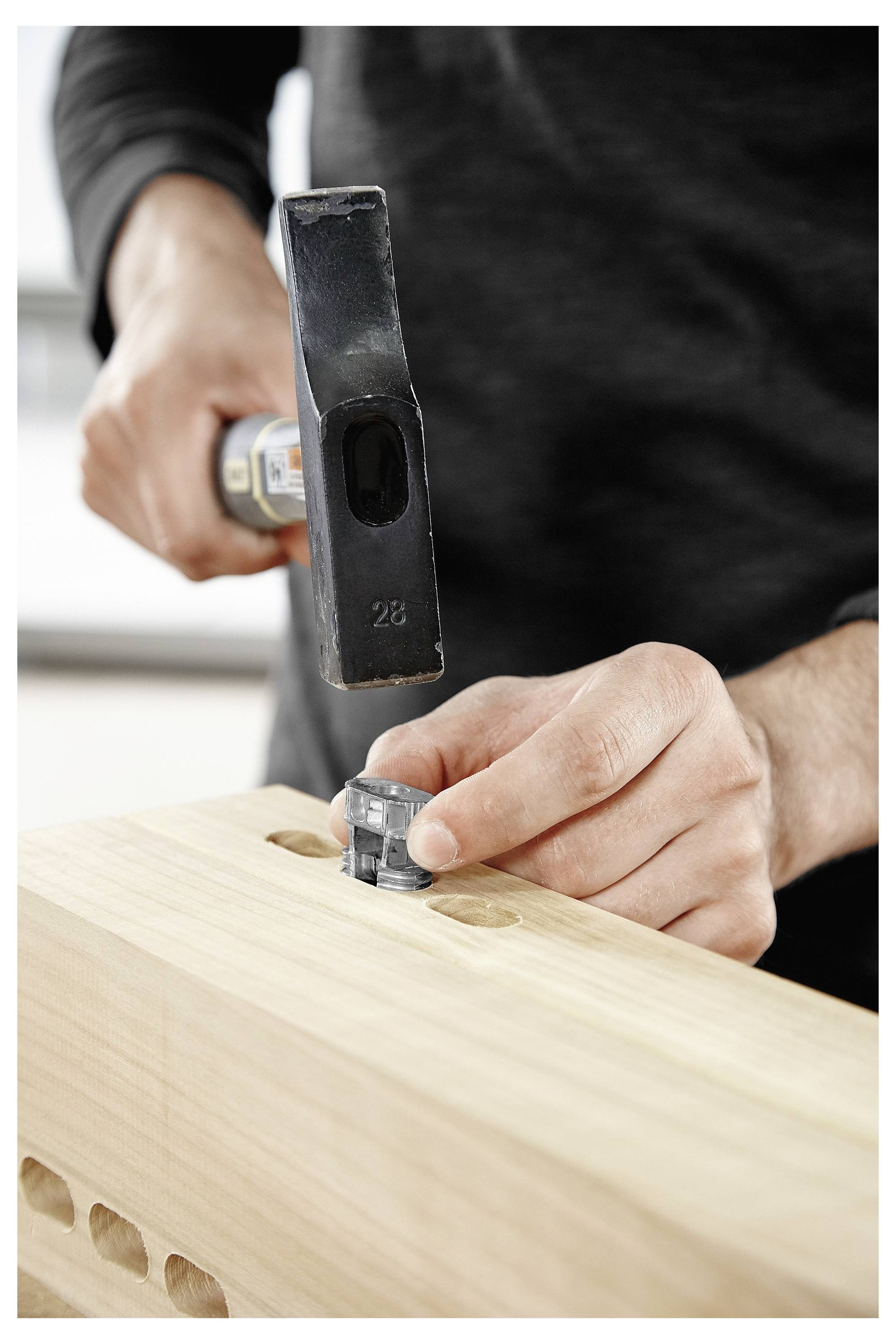 A person uses a hammer to insert a wooden dowel into a workbench hole, showcasing woodworking assembly in progress.