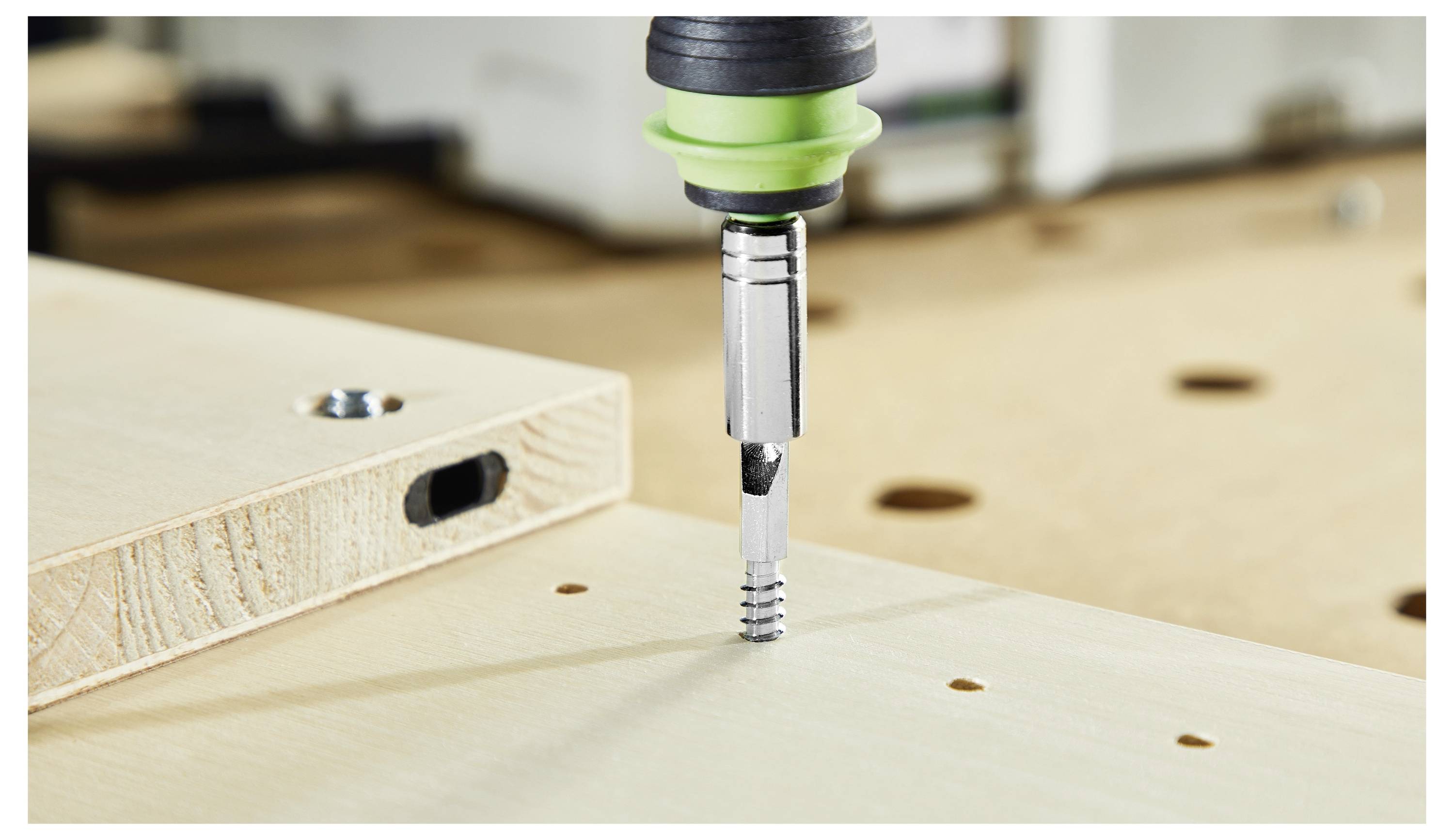 A screwdriver attaching a metal screw into a wooden surface, with multiple pre-drilled holes visible, suggesting assembly in progress.