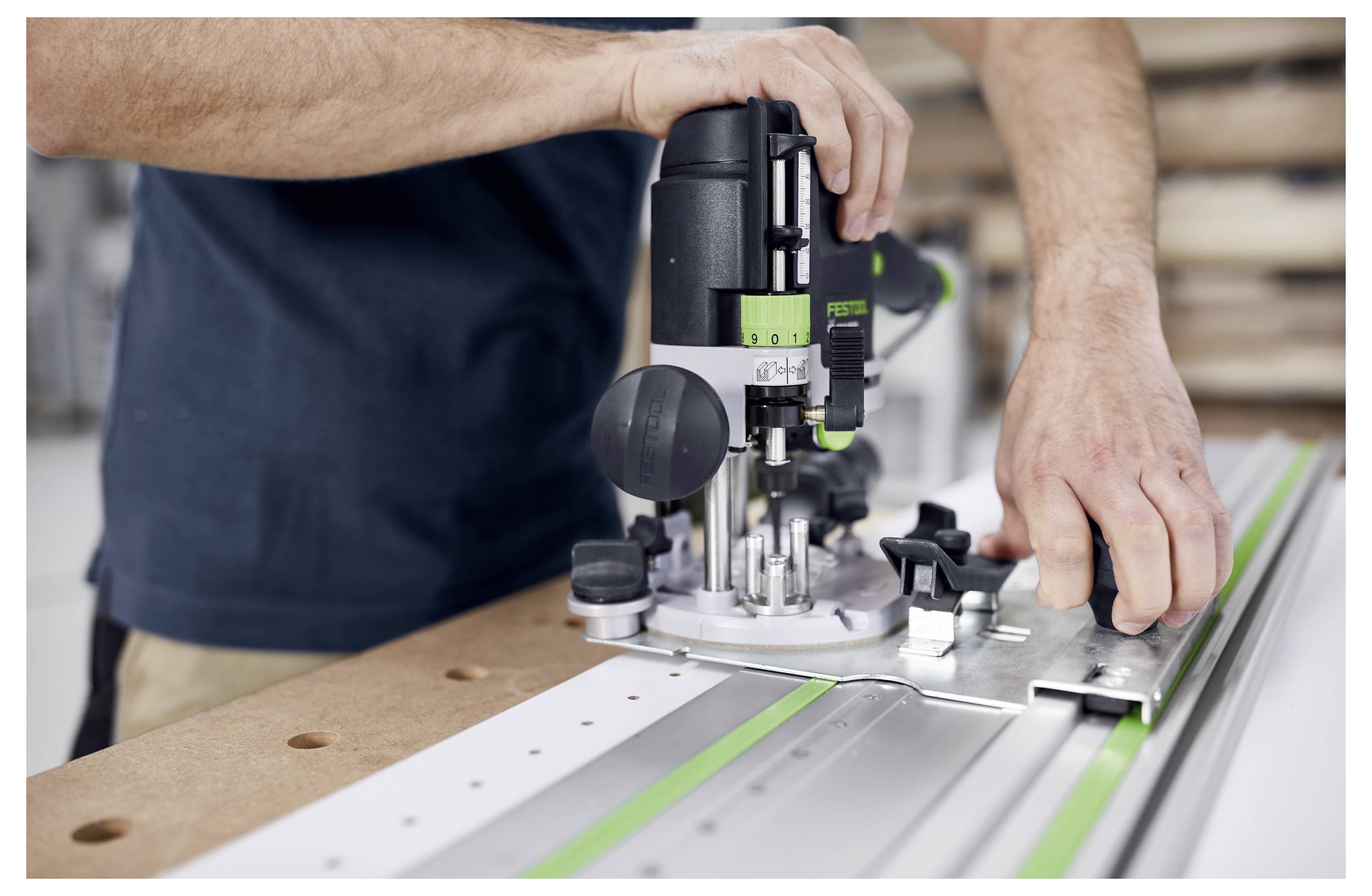 Person using a power tool to cut wood along a metal guide rail, focusing on precision and alignment in a workshop setting.