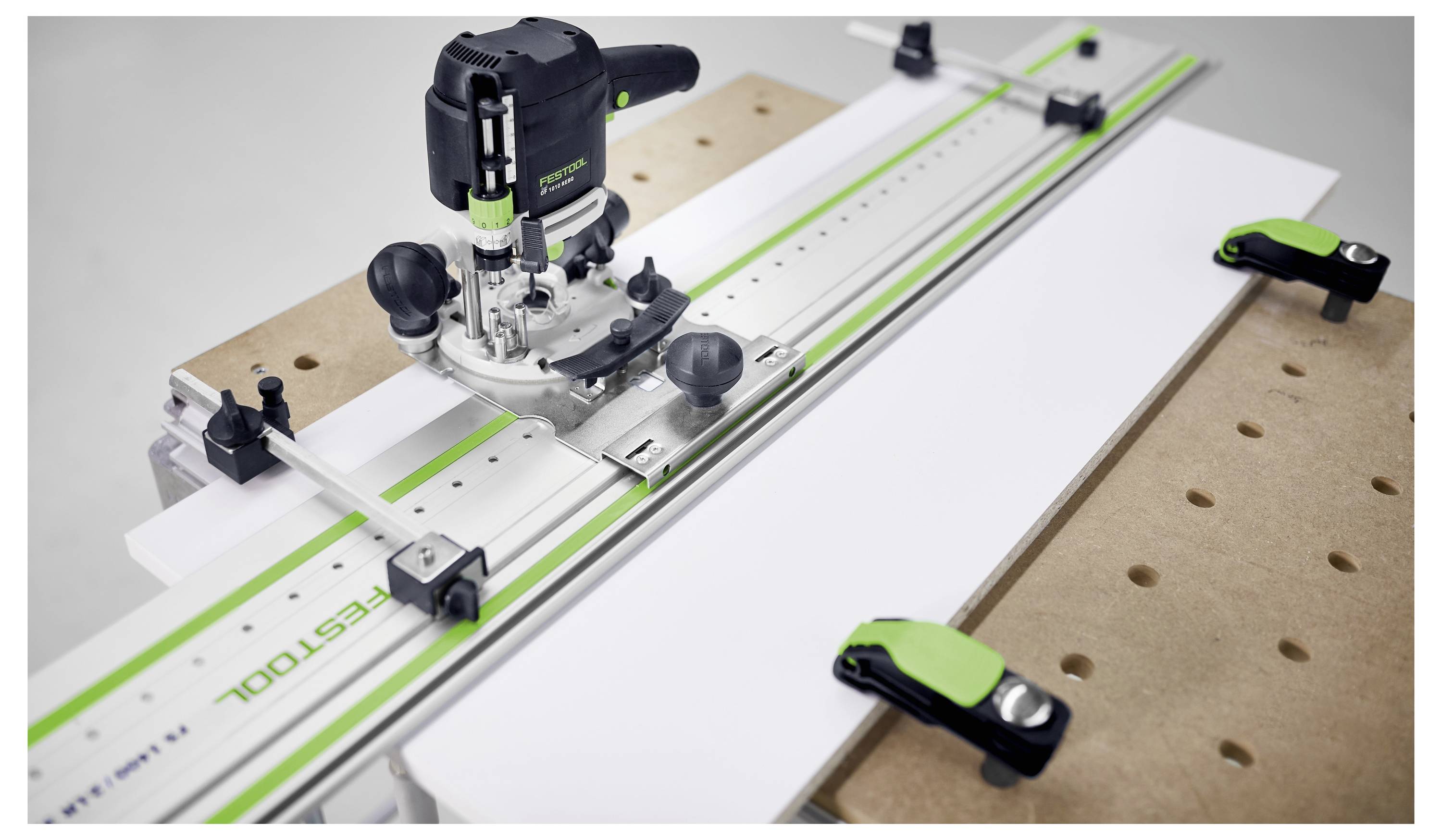 A router attached to a Festool guide rail system on a workbench, with clamps securing the material, demonstrating precision woodworking.