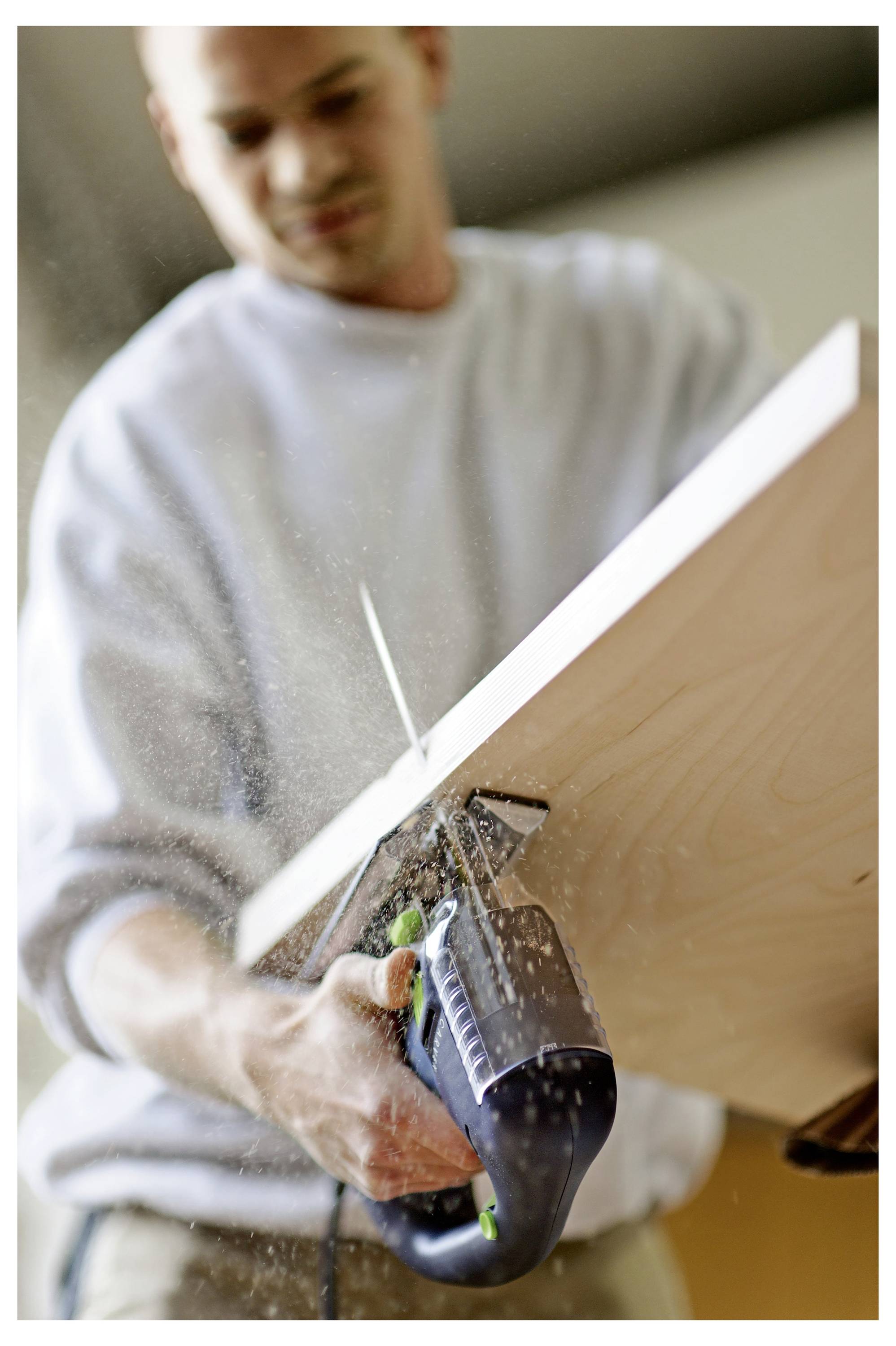 Man using an electric saw to cut a wooden plank. Sawdust is visible as the tool moves through the wood.