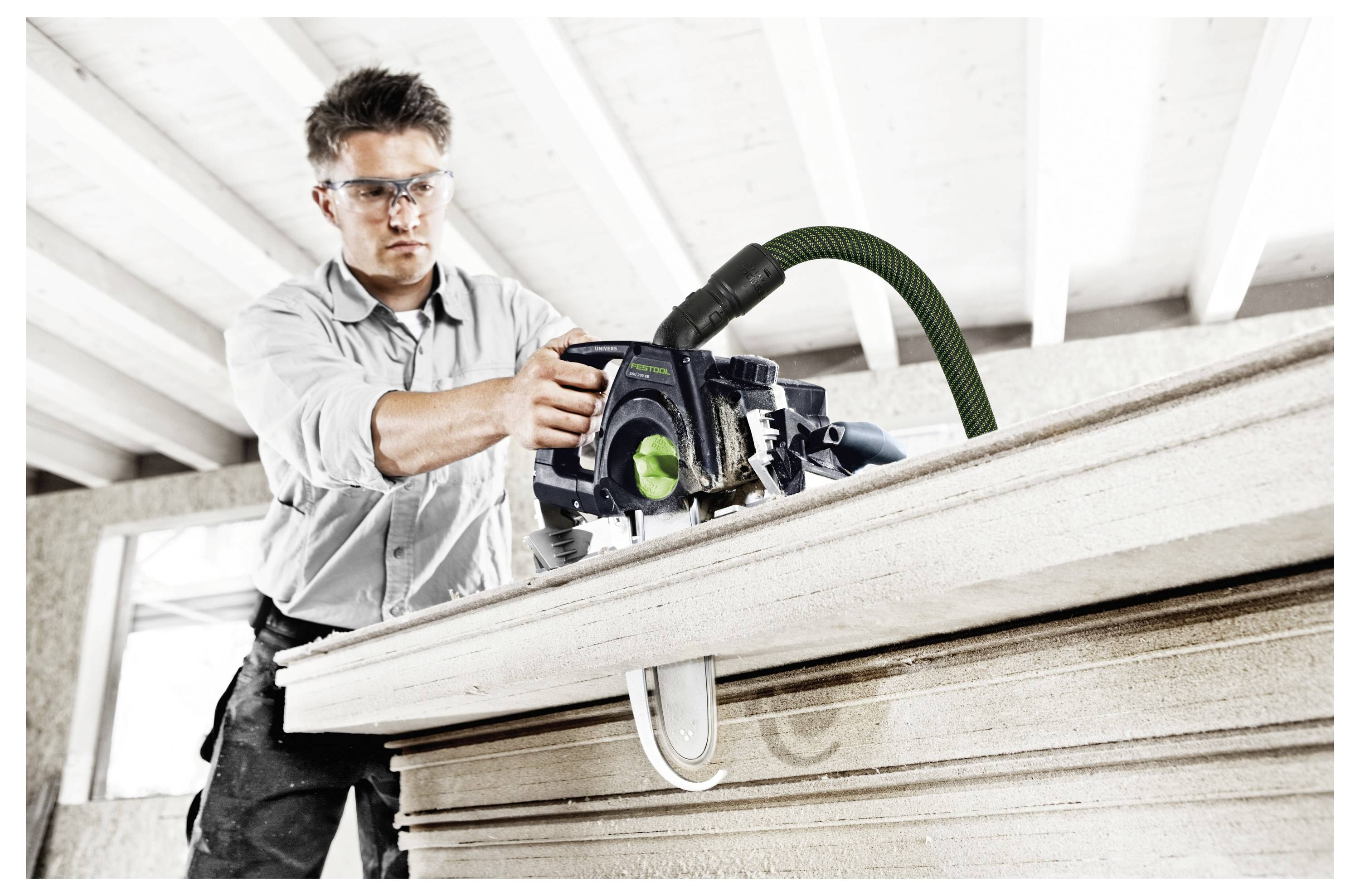 A person wearing safety goggles is using a circular saw to cut through thick wooden boards in a workshop setting.