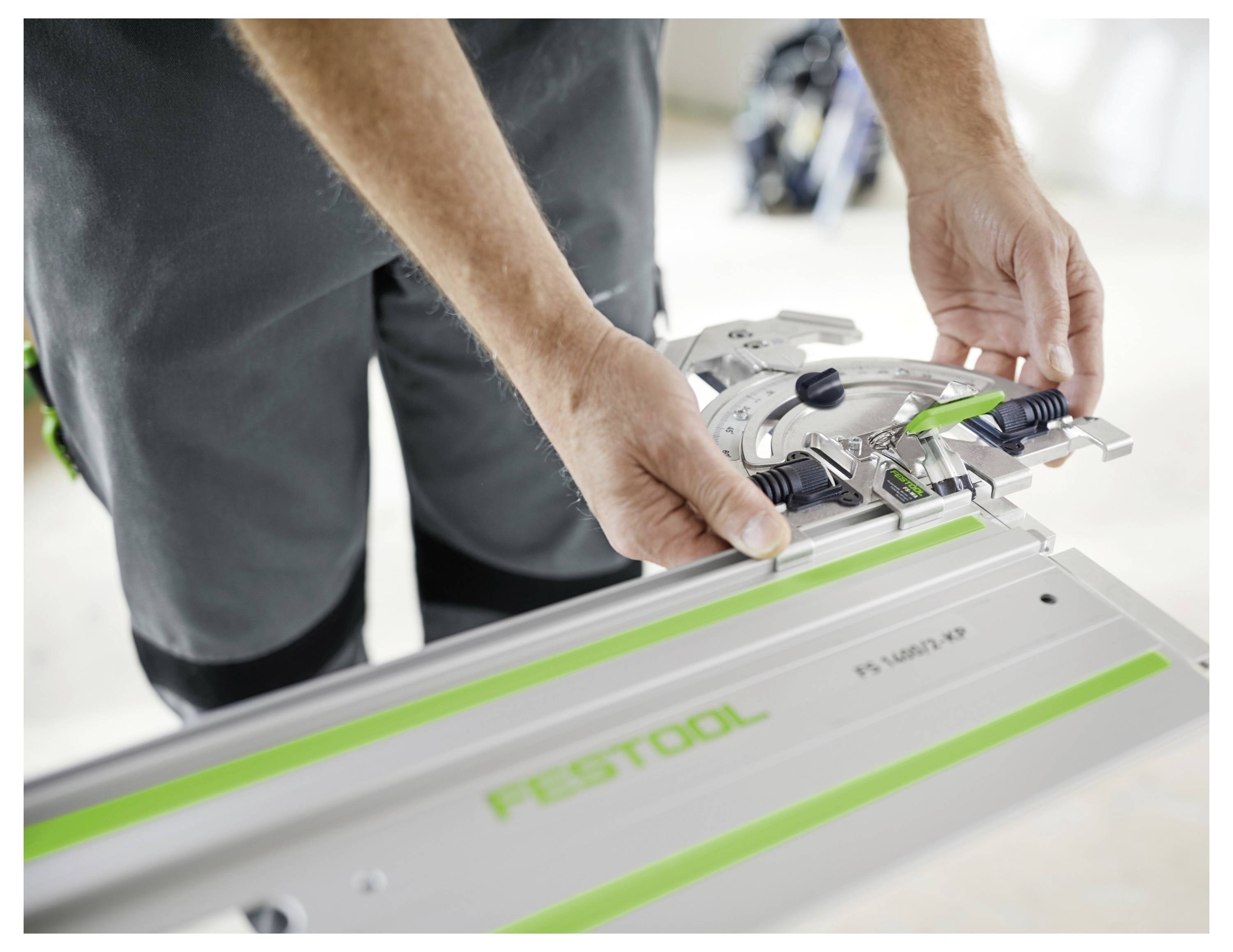 Close-up of a person adjusting a Festool guide rail system, showing hands securing the rail for precise cutting.