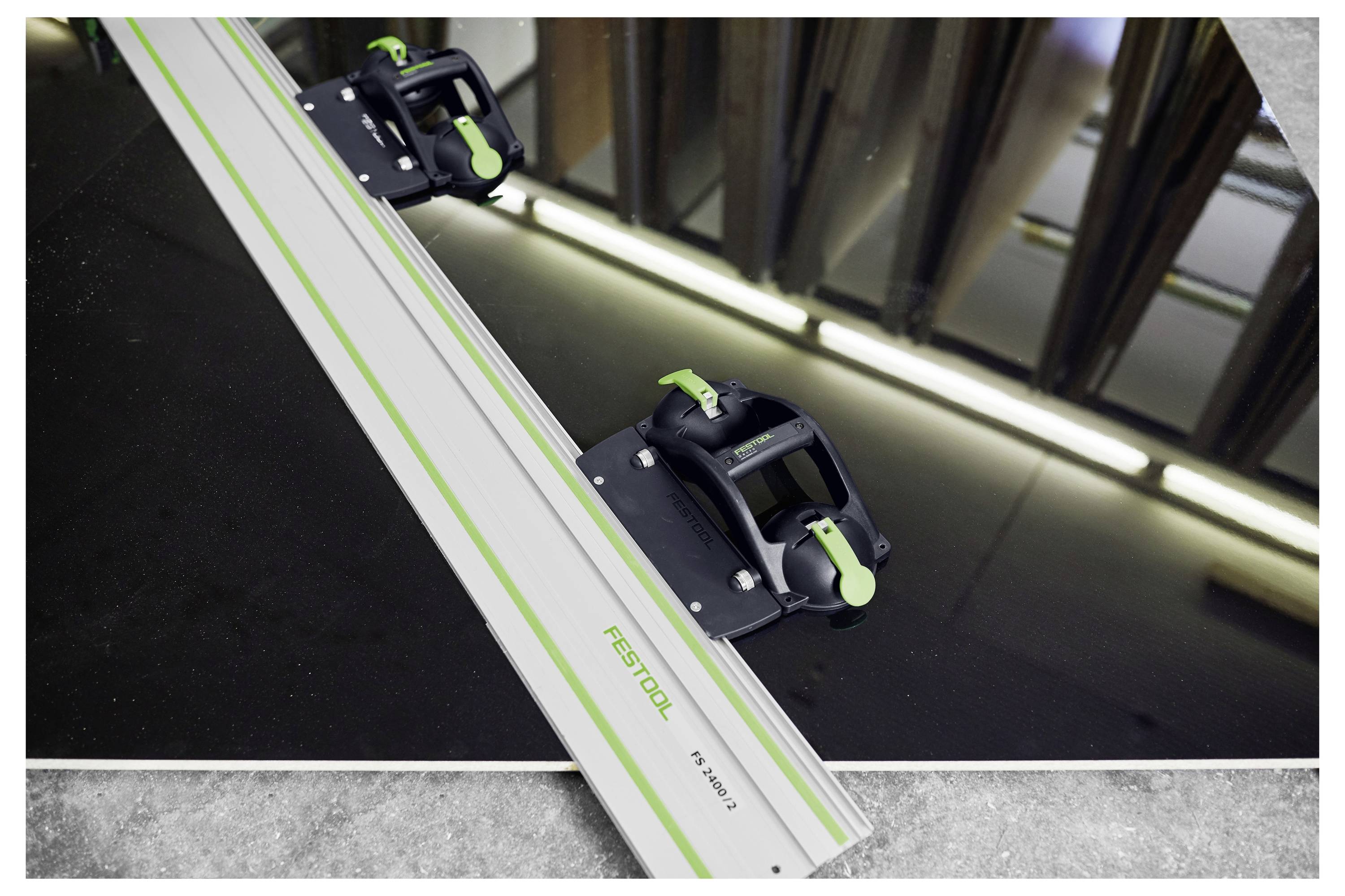 A metal guide rail with green accents, branded 'Festool', is aligned on a reflective dark surface inside a workshop setting.