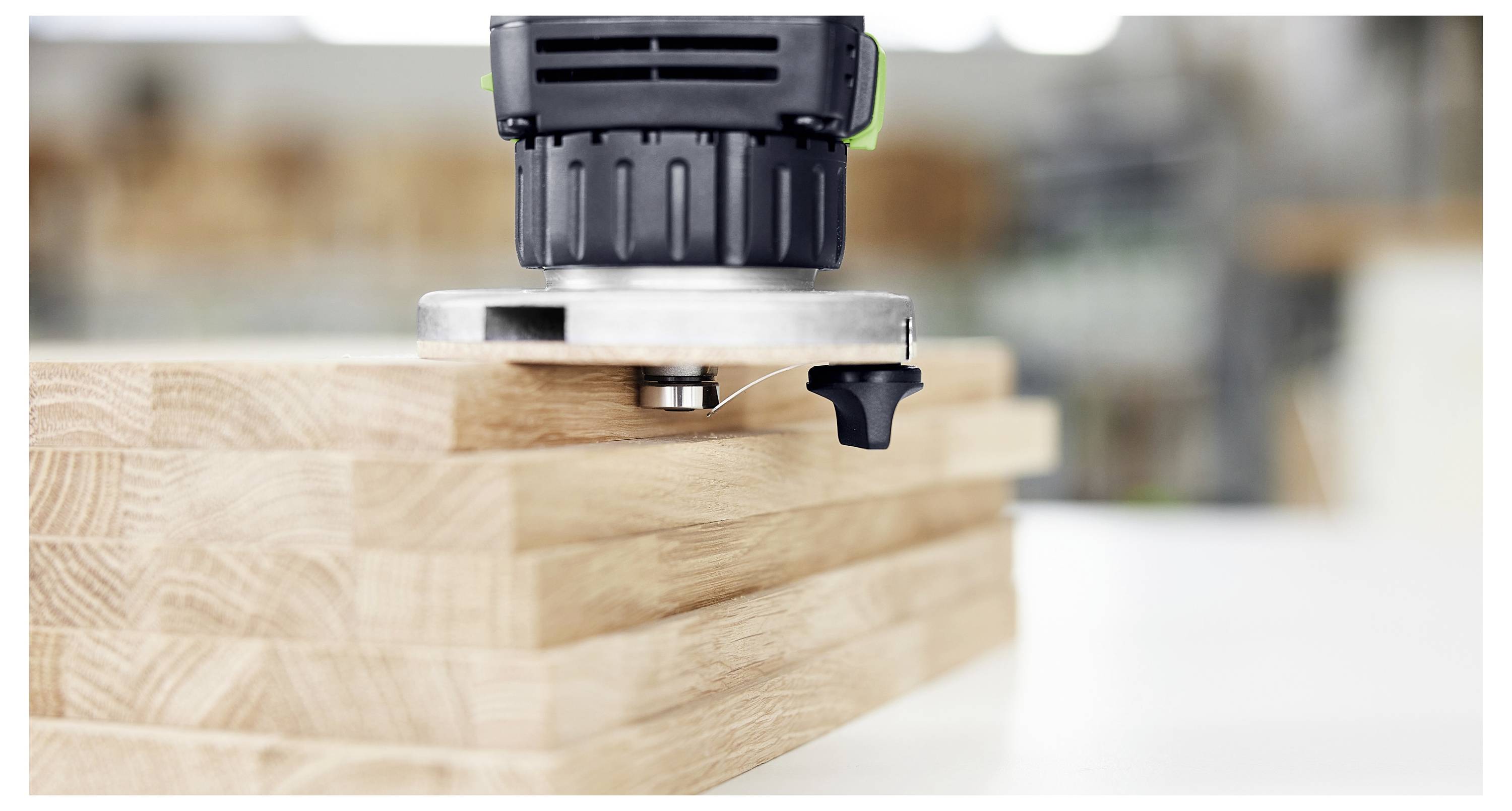 A wood router working on a stack of wooden boards on a white table in a workshop setting.