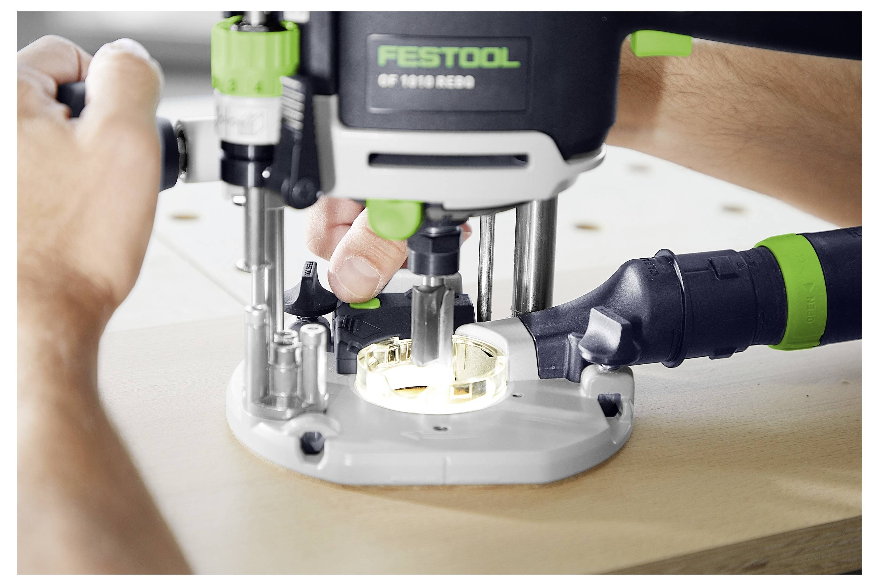 A person uses a Festool router to cut a circular groove into a wooden surface, demonstrating precise woodworking technique.