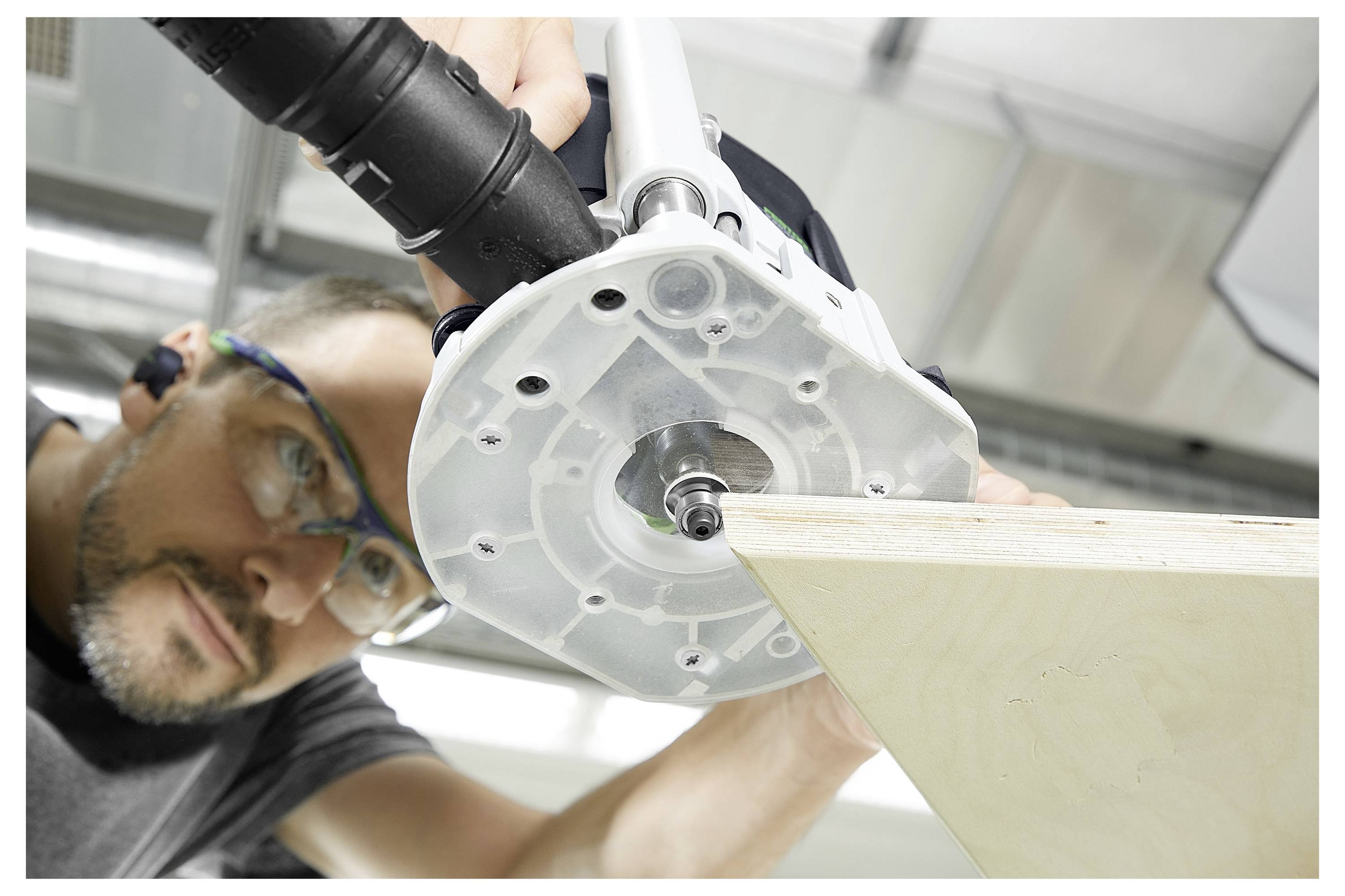 A person wearing safety goggles operates a power tool to shape the edge of a wooden board in a workshop setting.