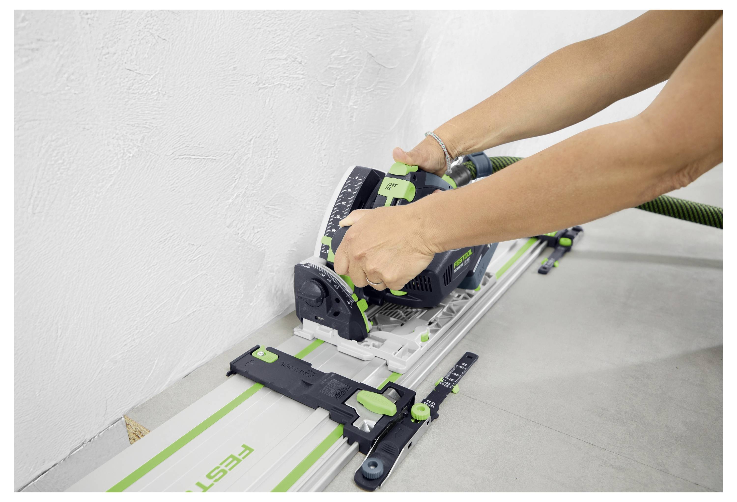 A person uses a circular saw on a guide rail to cut a wooden board. The tool is green and black, designed for precision cutting.