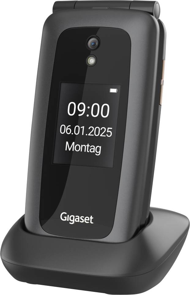 A digital display shows the date '06.01.2025' and time '09:00' on a closed flip phone standing in a charging dock.
