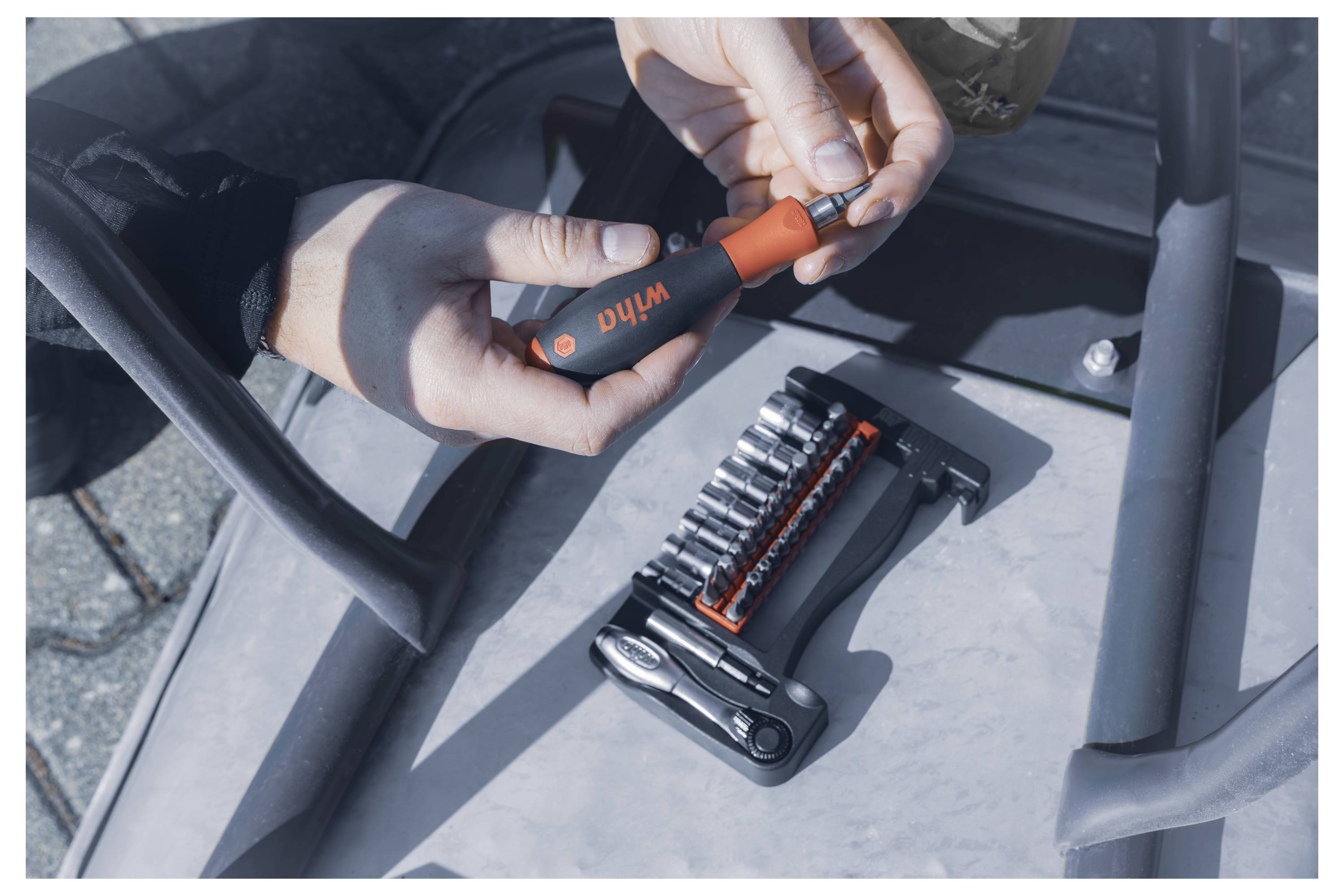 Person using a Wiha screwdriver to adjust a tool set on a metal surface. Various tool bits and sockets are organized in a holder nearby.